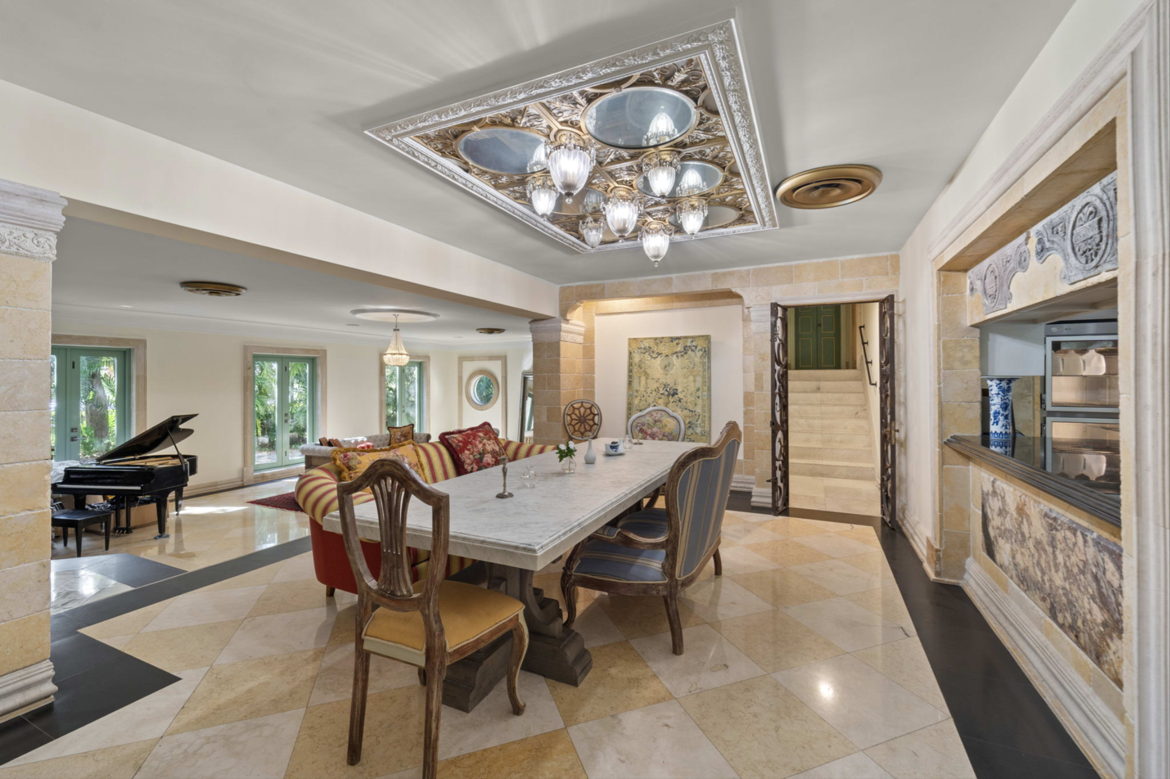 The image shows a spacious dining area with a marble table surrounded by upholstered chairs, large windows, and a grand piano in the corner.