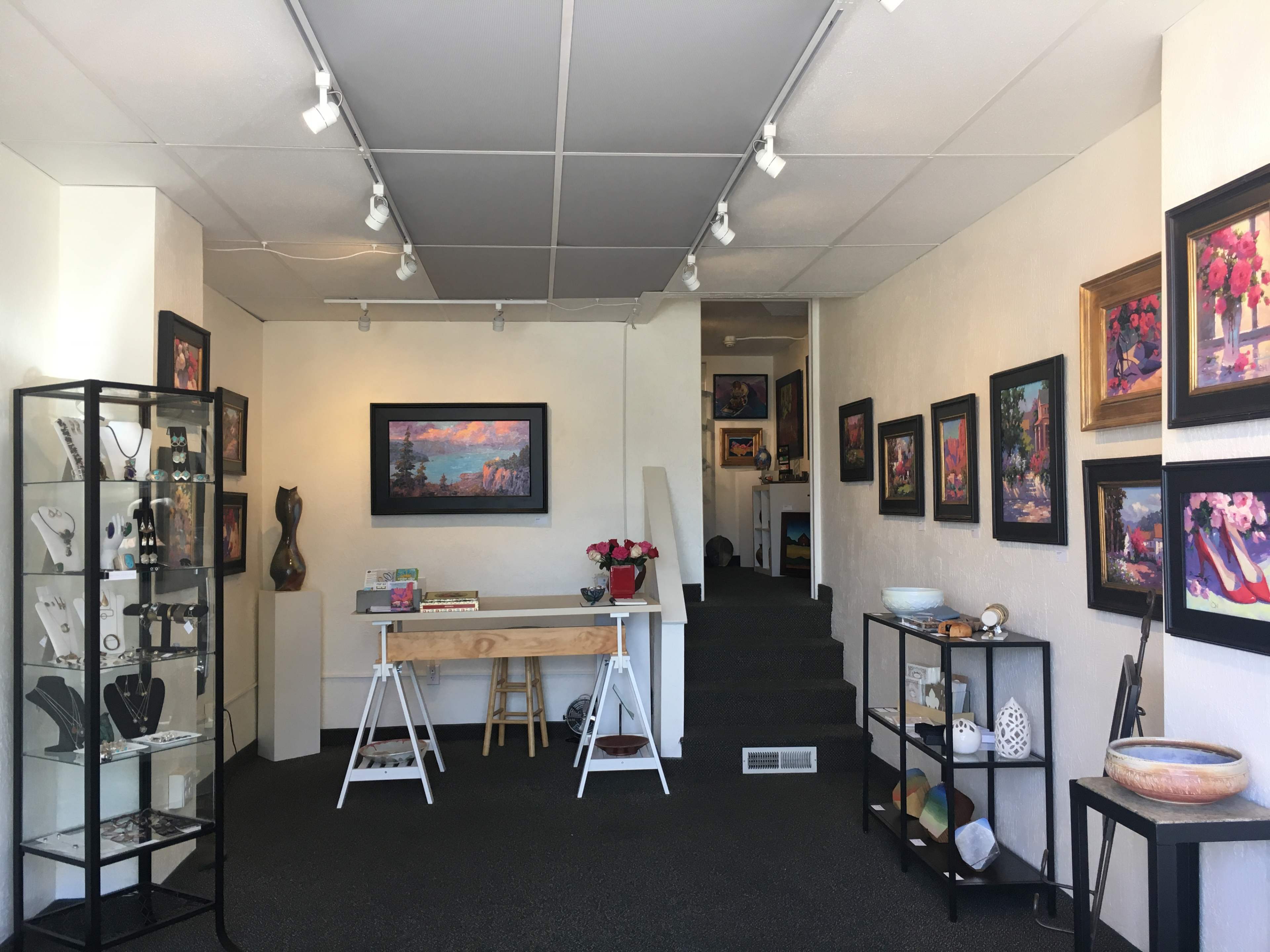 The interior of an art gallery featuring framed paintings on the walls, display cases with jewelry, and various artistic items throughout the space.
