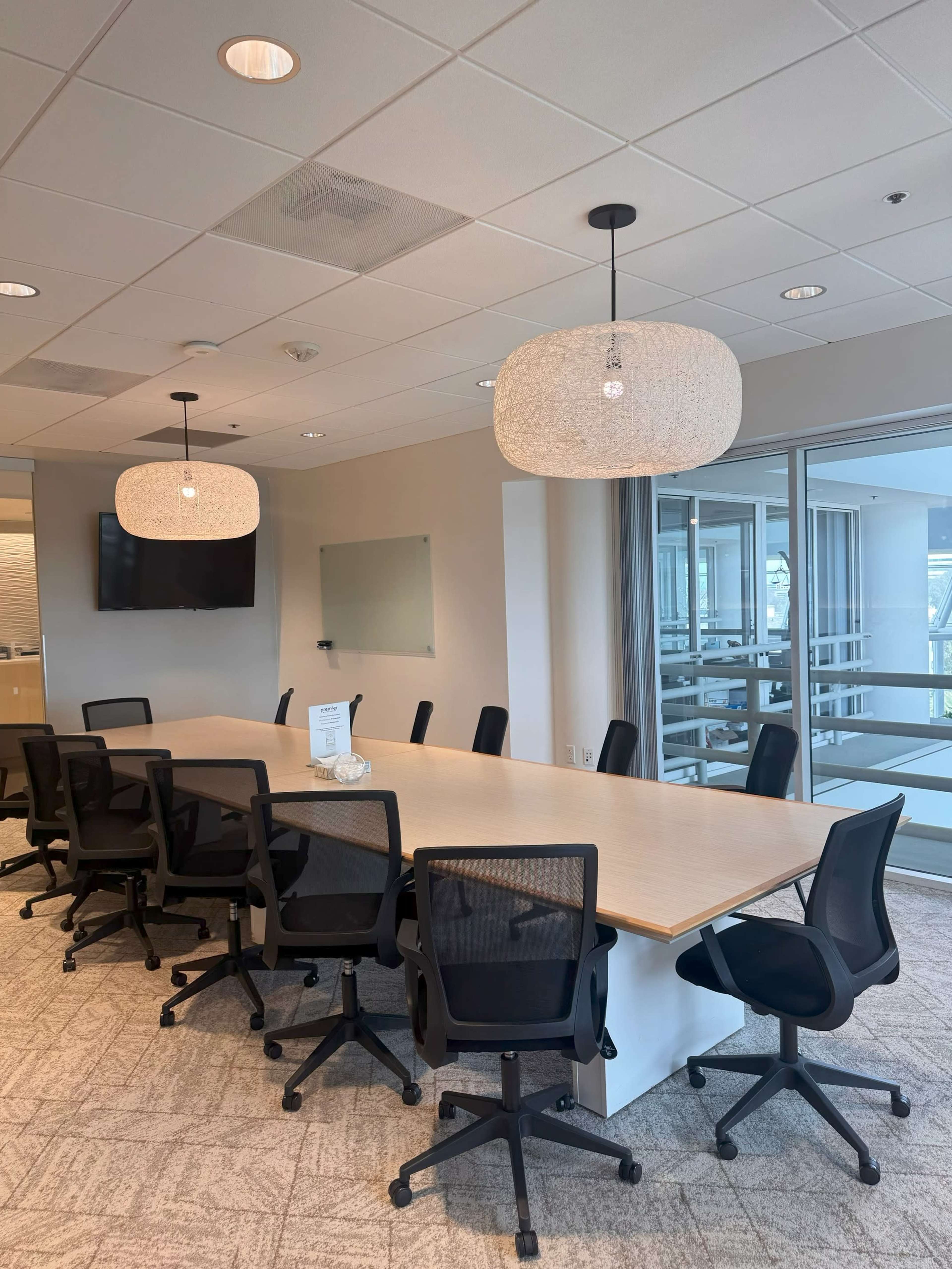 The image shows a modern conference room with a long table surrounded by black office chairs, illuminated by two pendant lights.