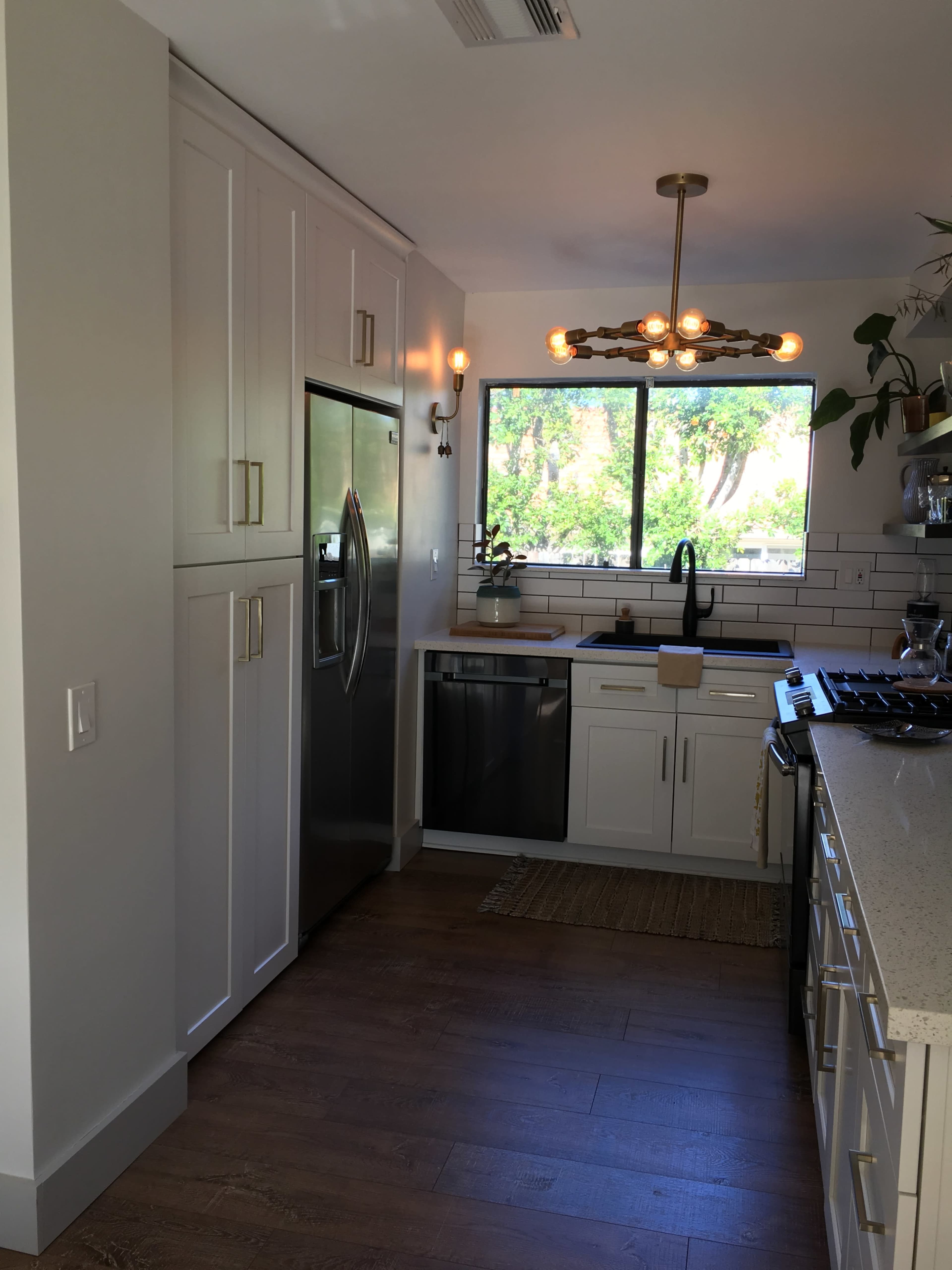 A modern kitchen with stainless steel appliances, light-colored cabinetry, and a window overlooking greenery.