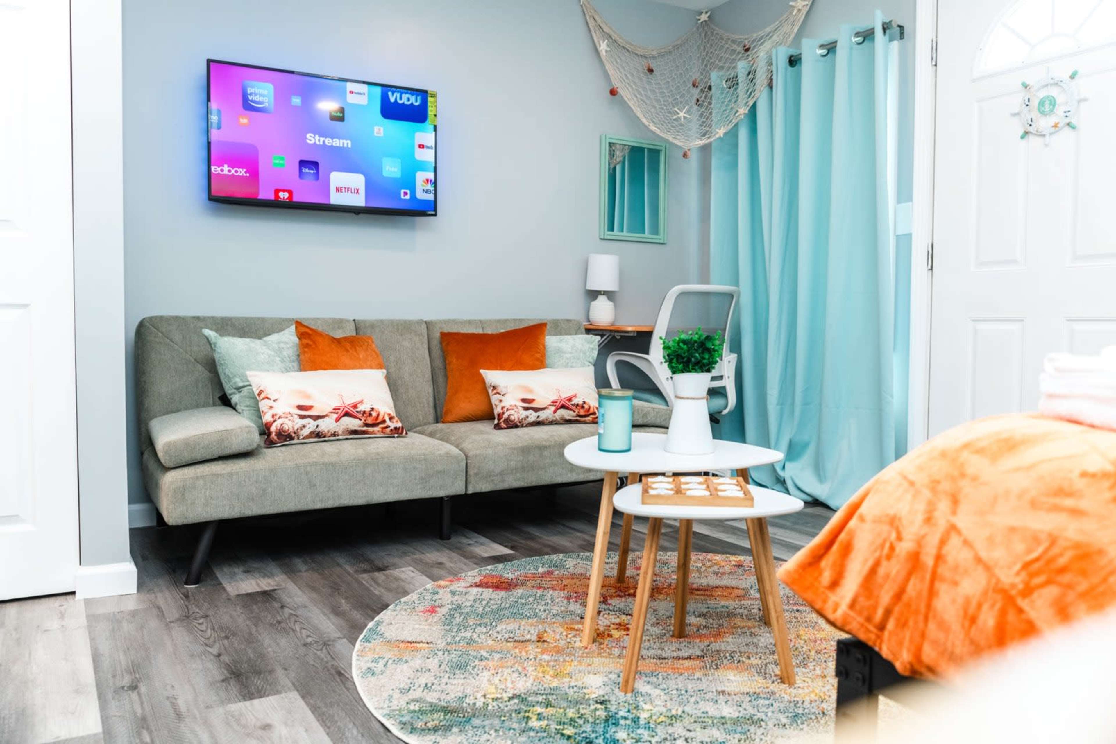 The image shows a cozy living space with a gray sofa, a small round coffee table, and a wall-mounted TV displaying streaming apps.