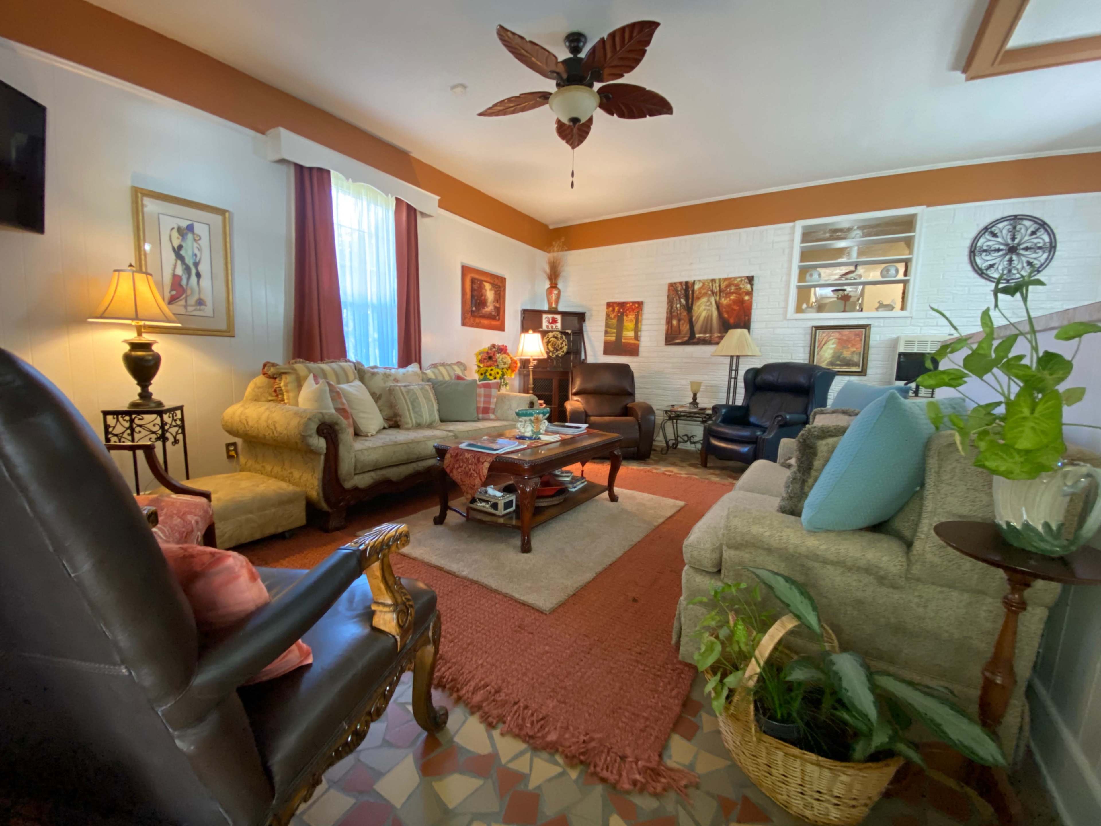 The living room features multiple seating areas with a mix of sofas and armchairs, a central coffee table, and decorative plants, all arranged around a warm, inviting ambiance.