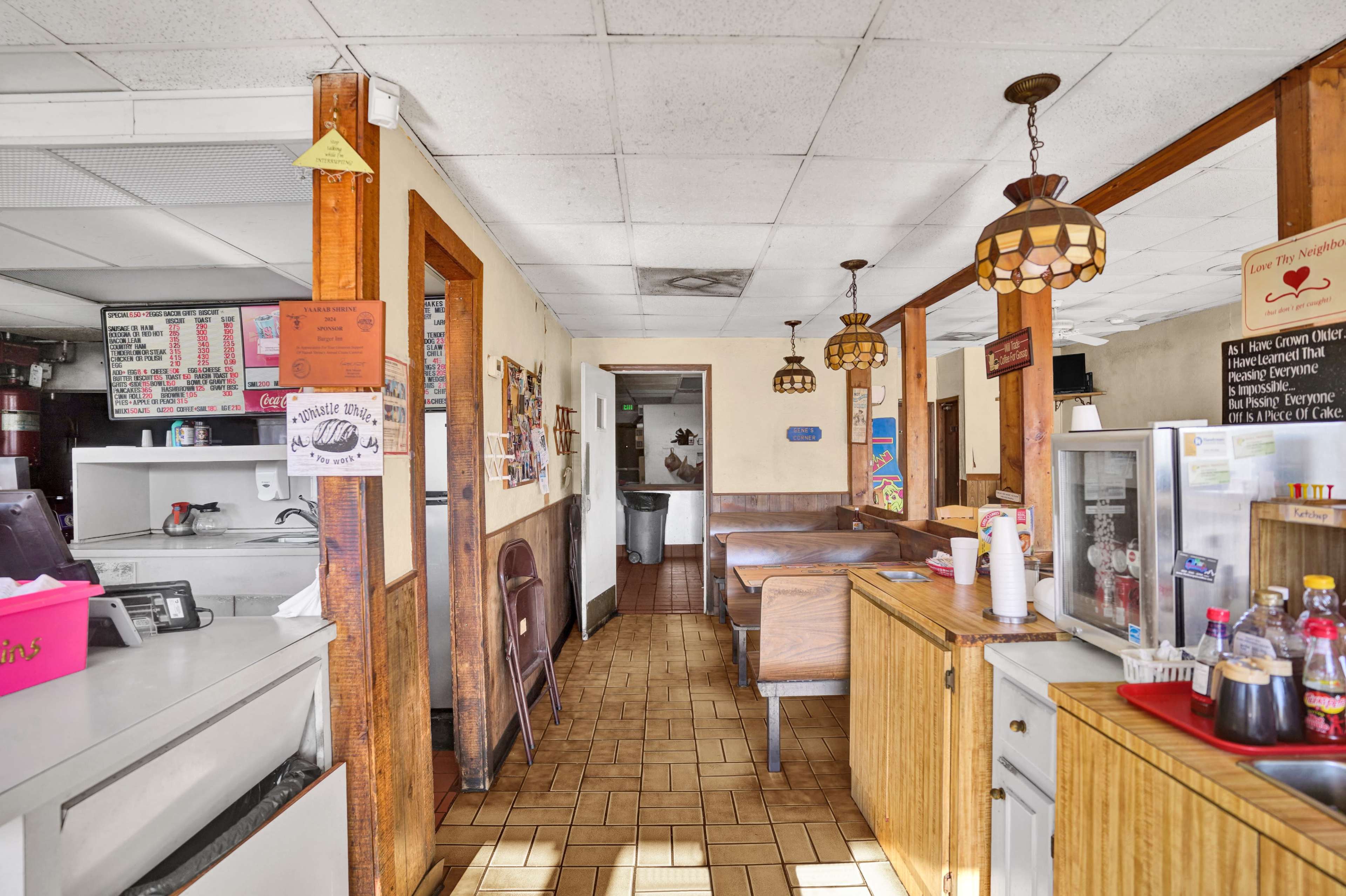 The image shows the interior of a diner featuring wooden furnishings, a counter with condiments, and booths along the walls.
