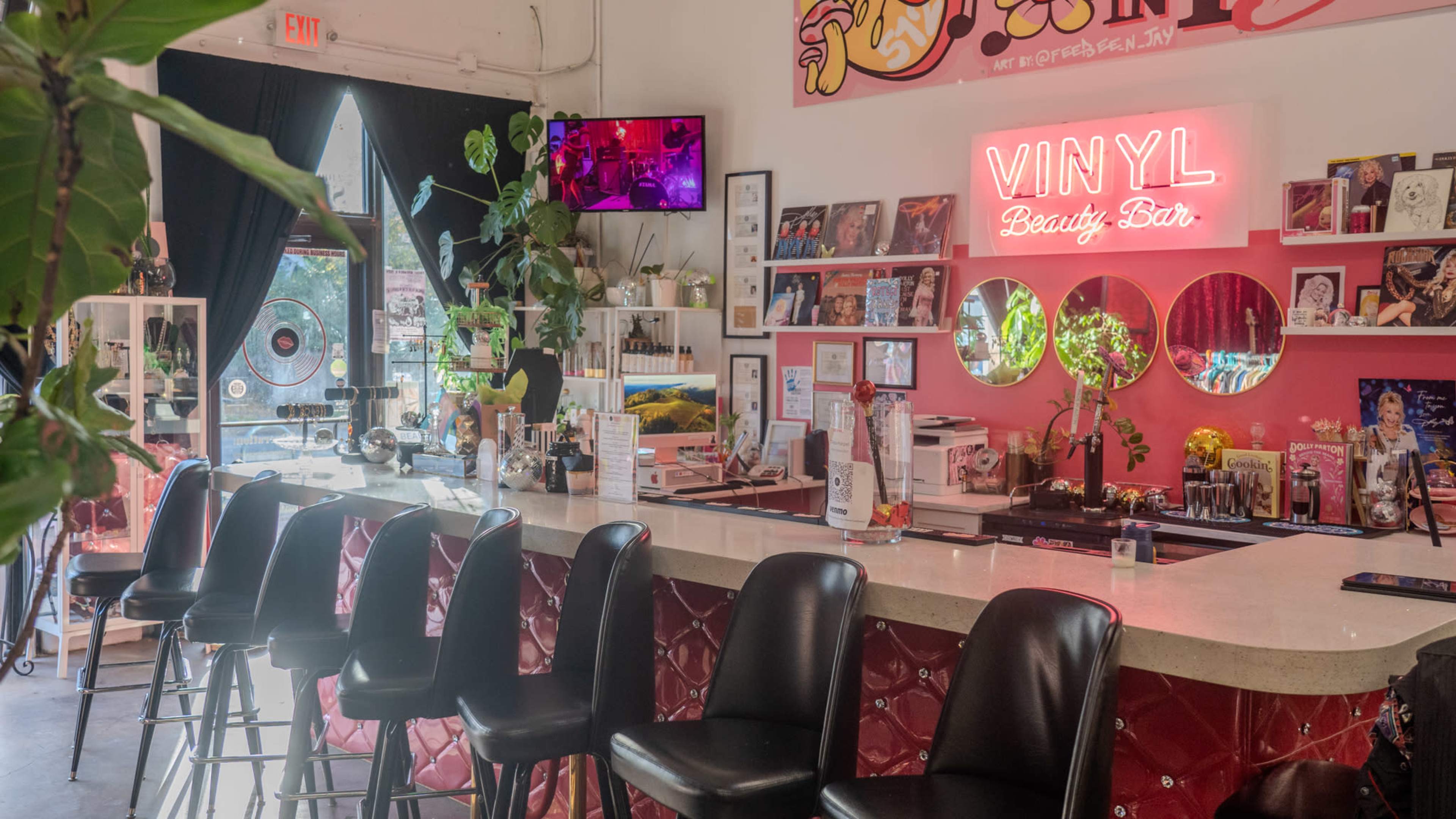 The image shows a vibrant beauty bar with a counter, black stools, and a neon sign that reads "VINYL," surrounded by shelves displaying various beauty products and decor.