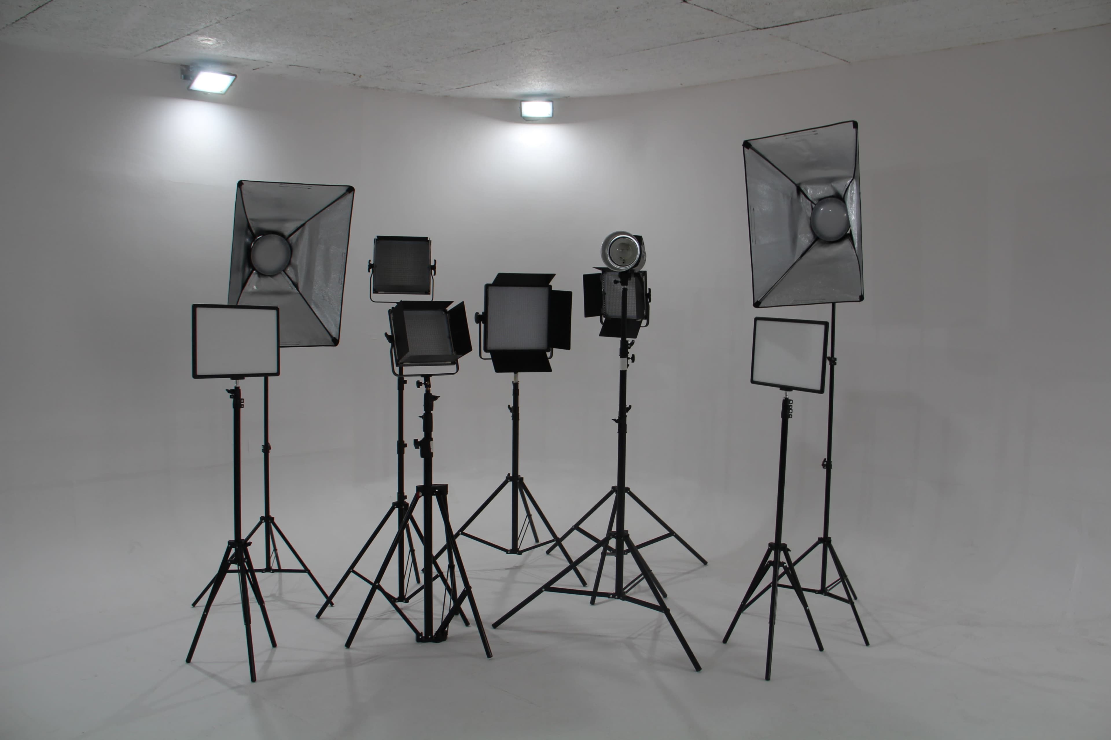 A set of studio lighting equipment arranged on tripods in a plain white room.