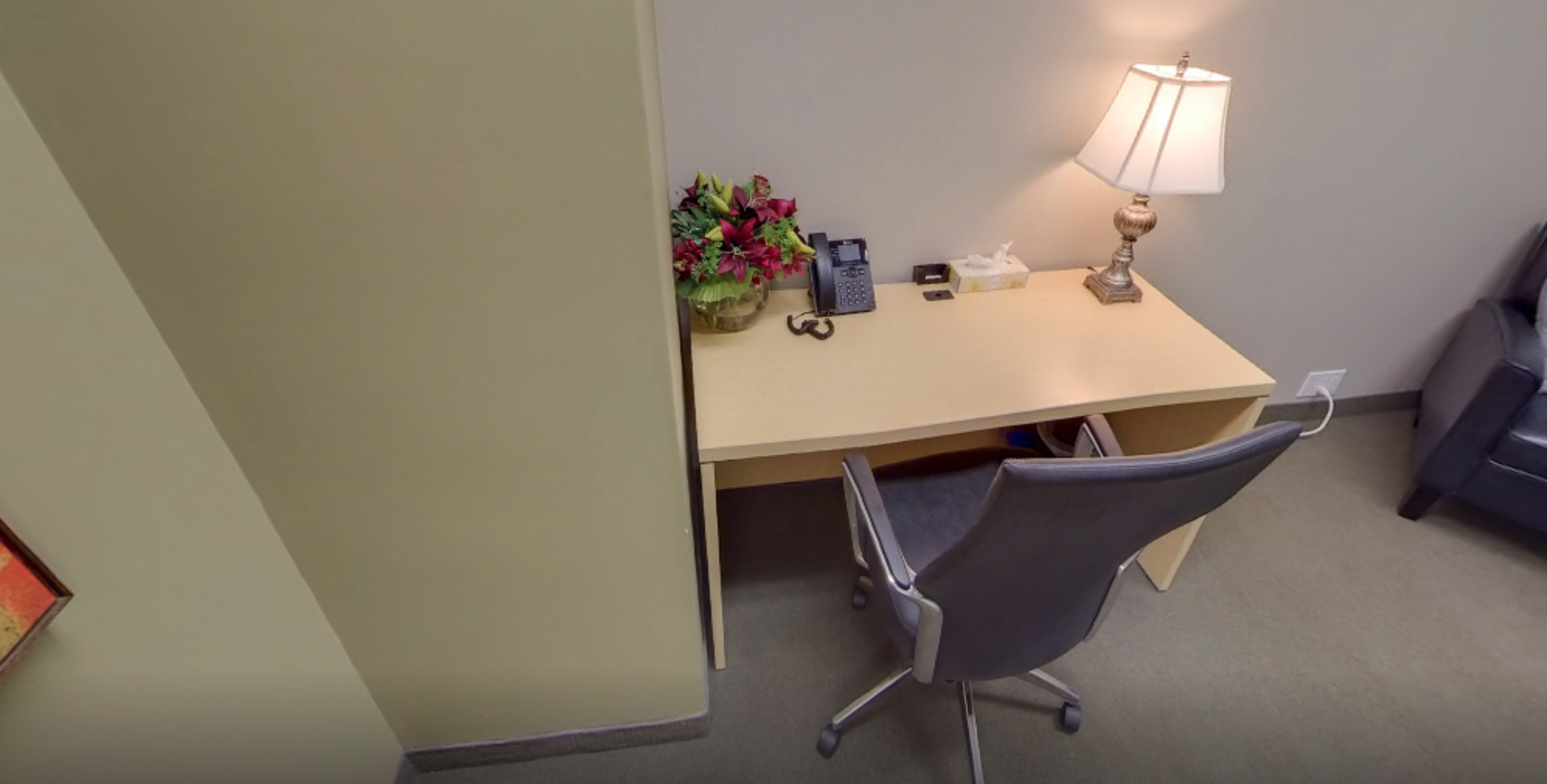 The image shows a simple desk with a chair, a lamp, a phone, a tissue box, a small decorative plant, and a pair of glasses arranged on the surface.