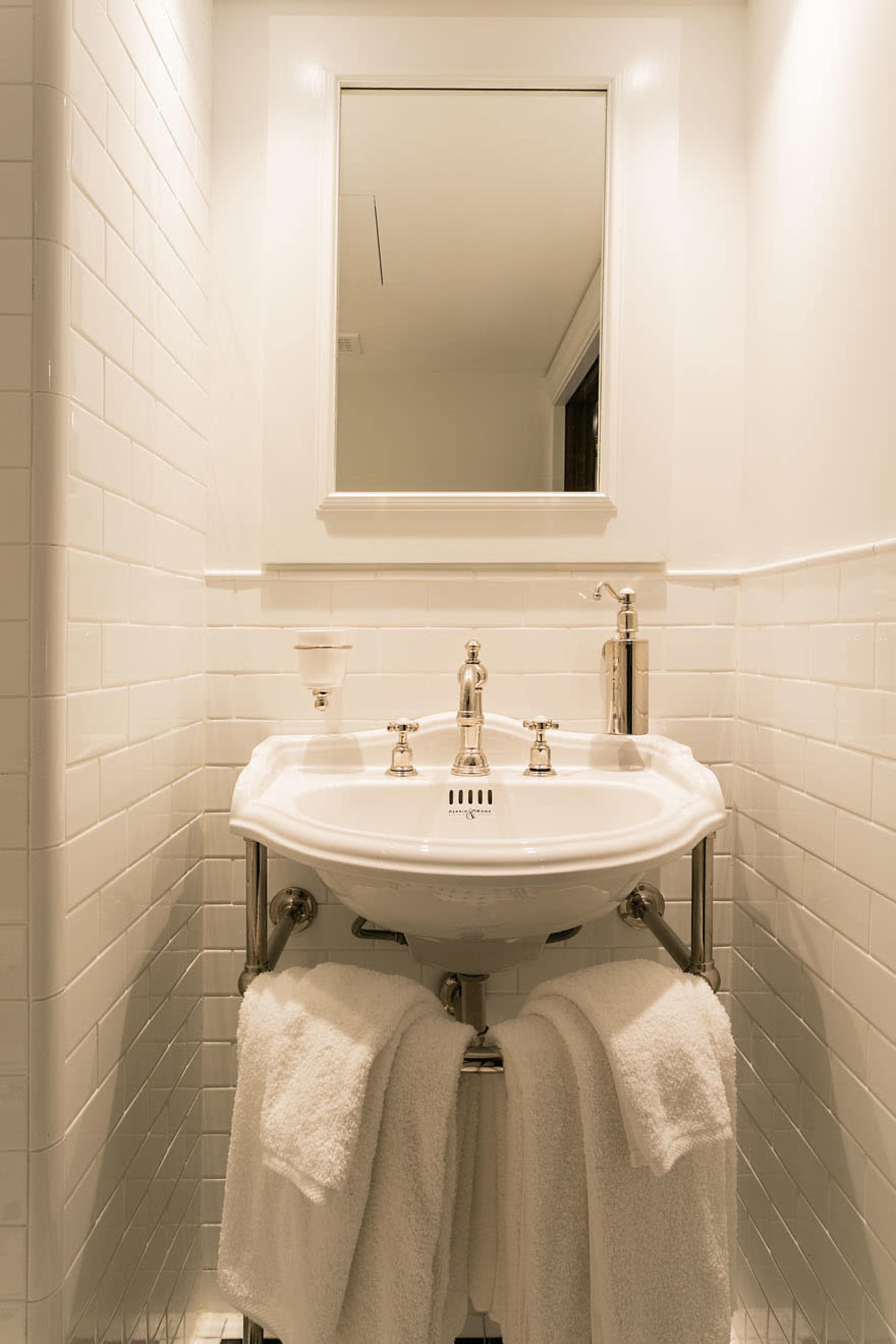 A white bathroom features a pedestal sink with a mirror above it, complemented by two towels hanging underneath.