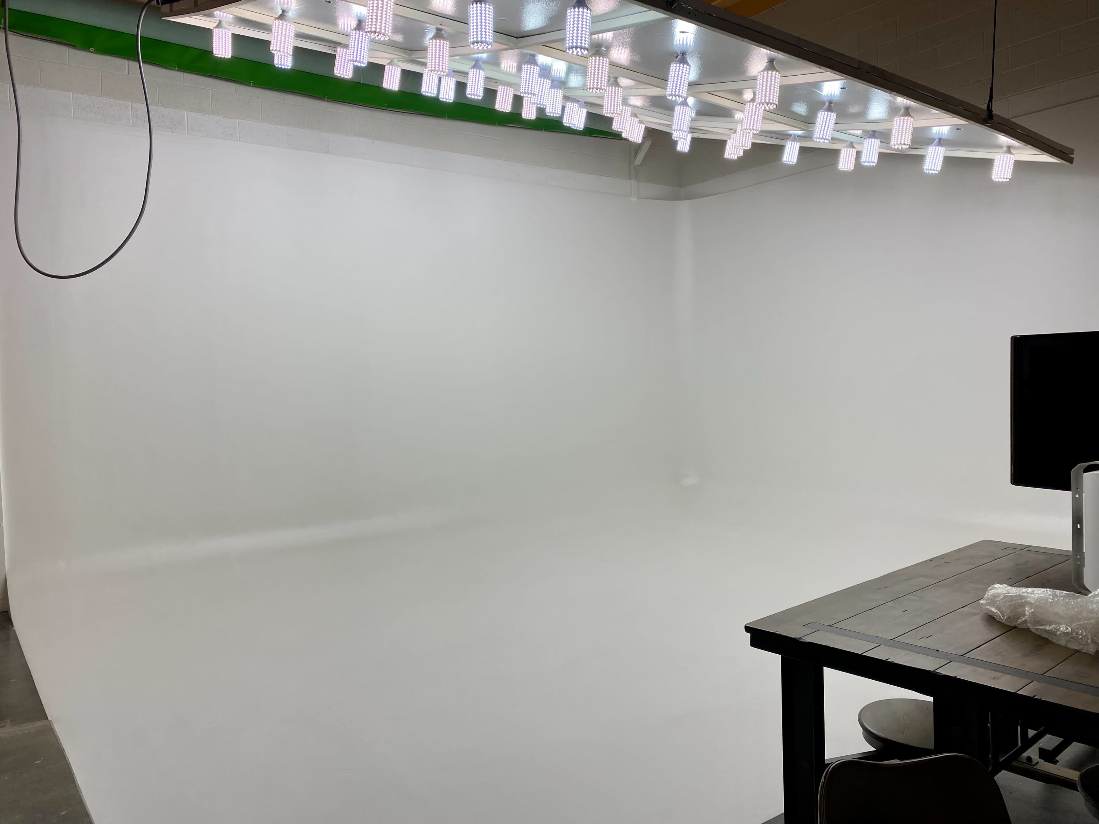 A spacious photo studio with white walls, a white backdrop, and overhead lighting.