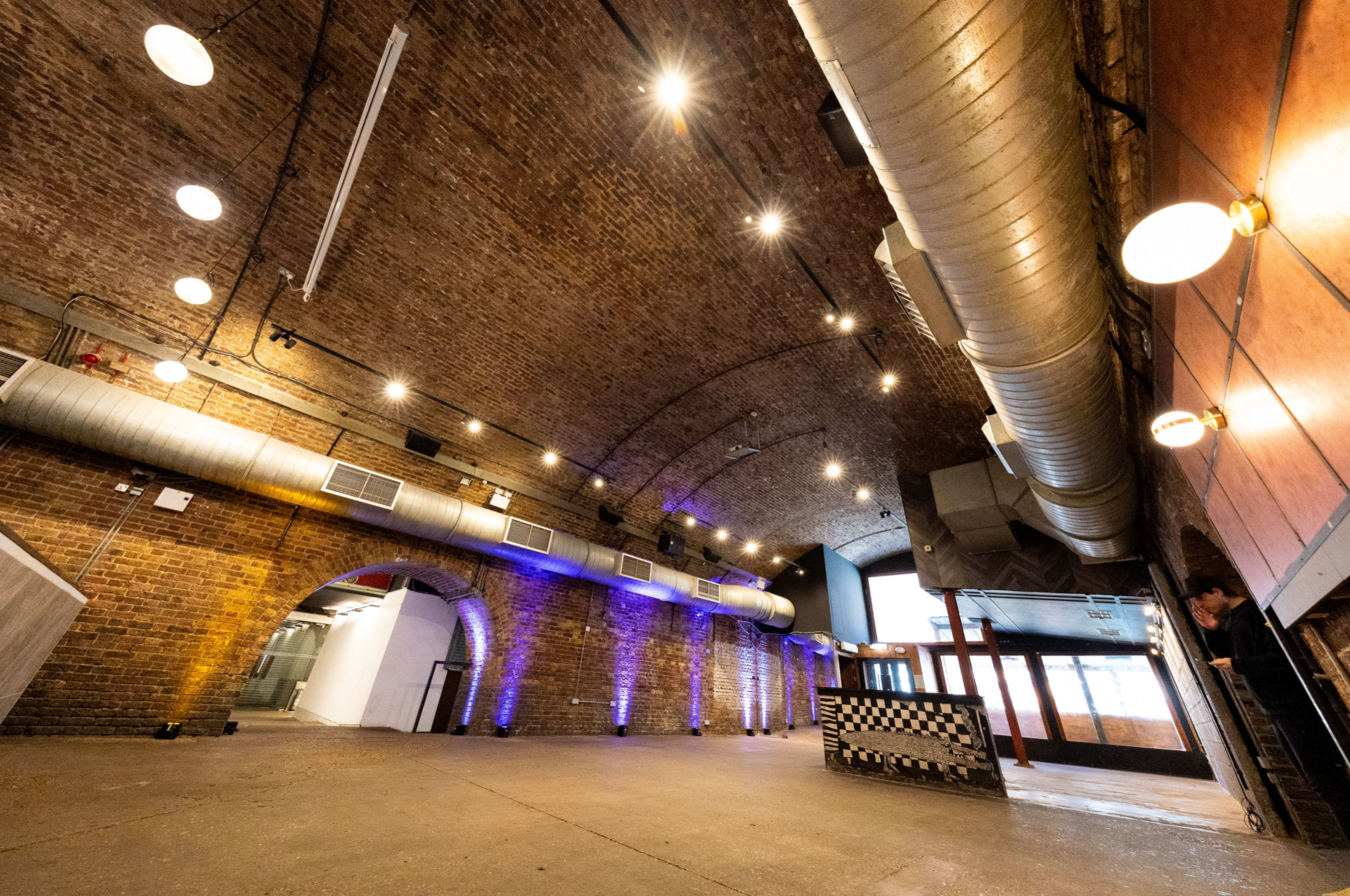 The image shows an industrial-style interior with a high arched brick ceiling, exposed ductwork, and several sources of overhead lighting.