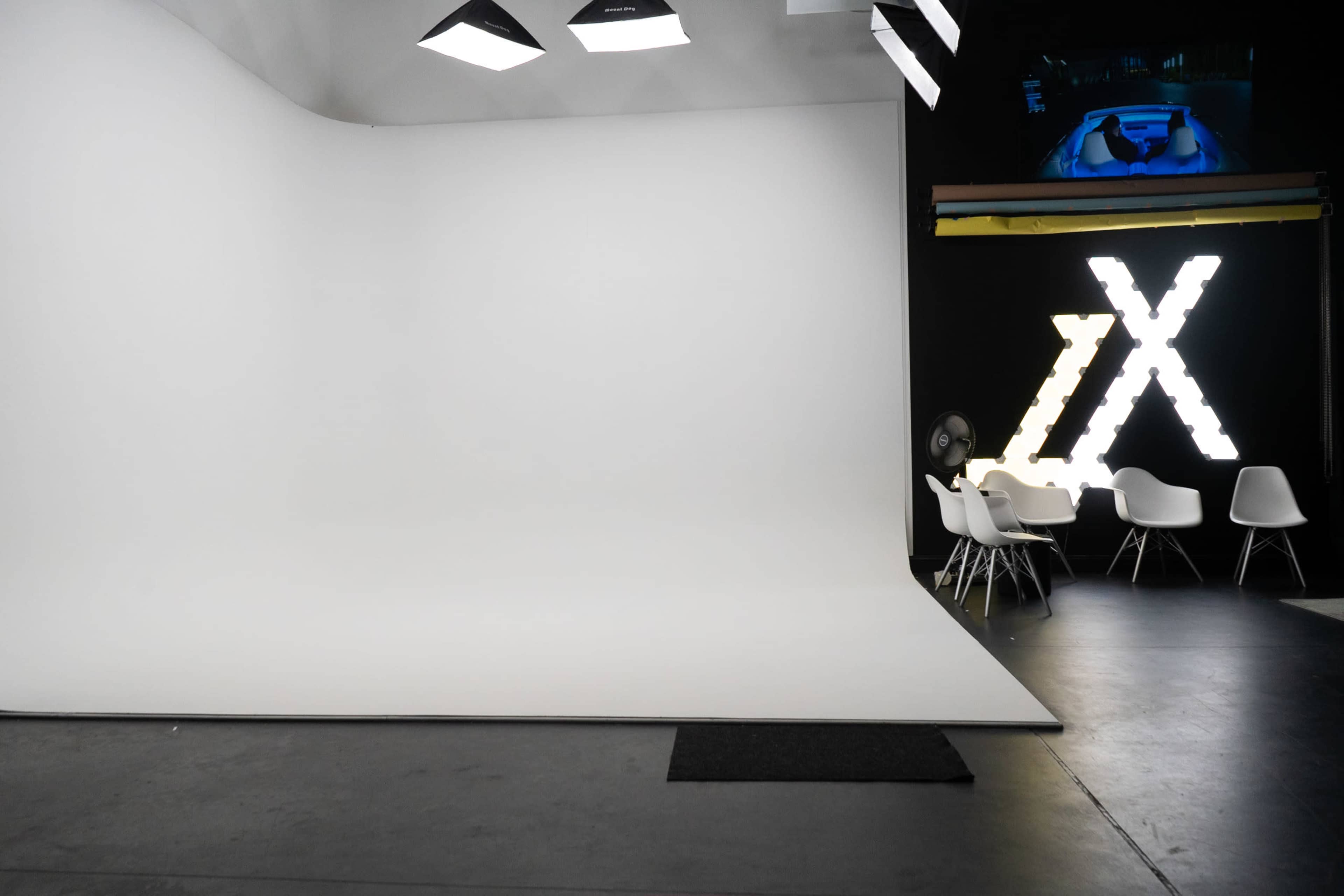 A minimalist studio space with a large white backdrop, modern chairs, and a lighted sign in the background.