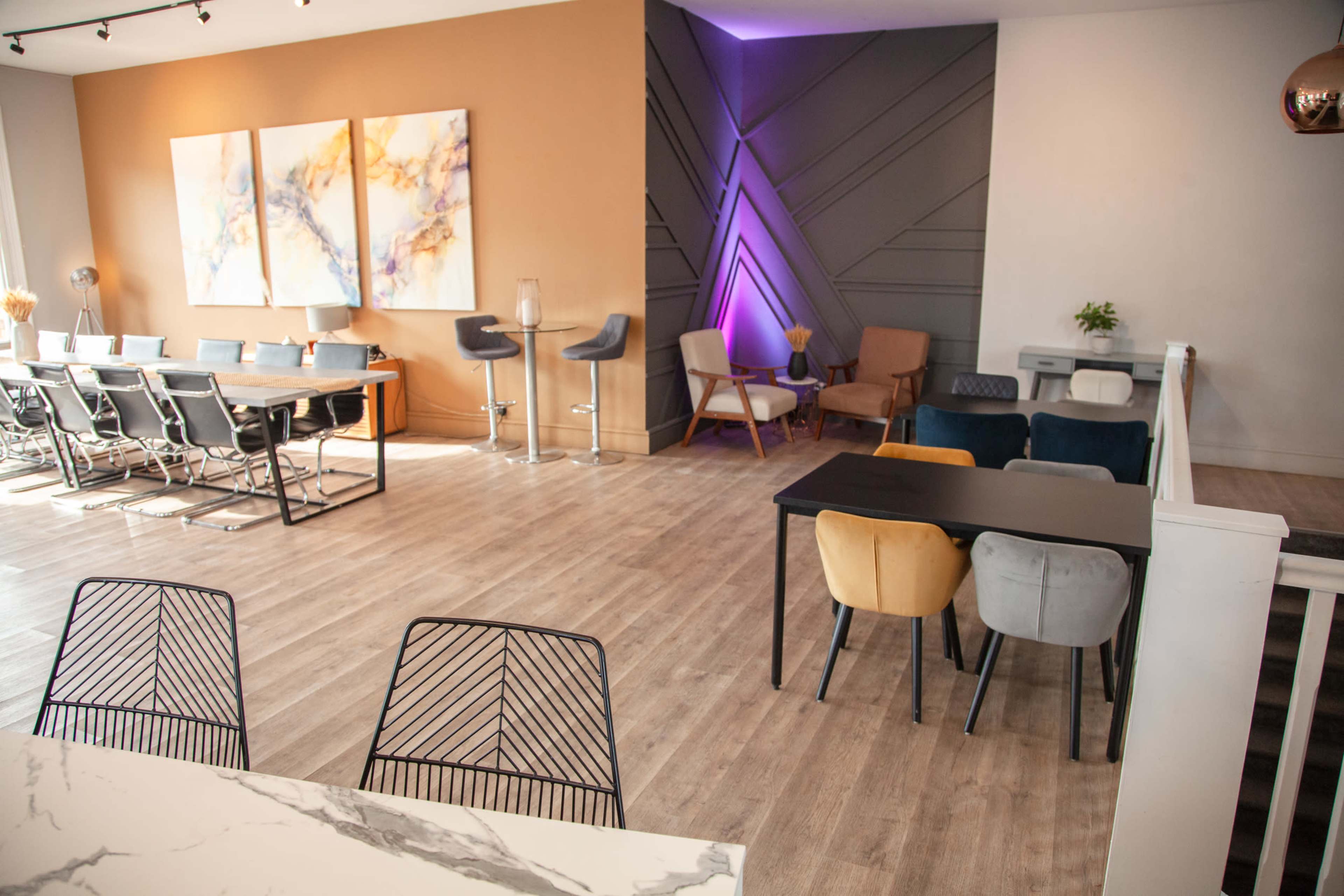 A spacious, modern interior features various seating arrangements, including tables and chairs, along with decorative wall art and ambient lighting.