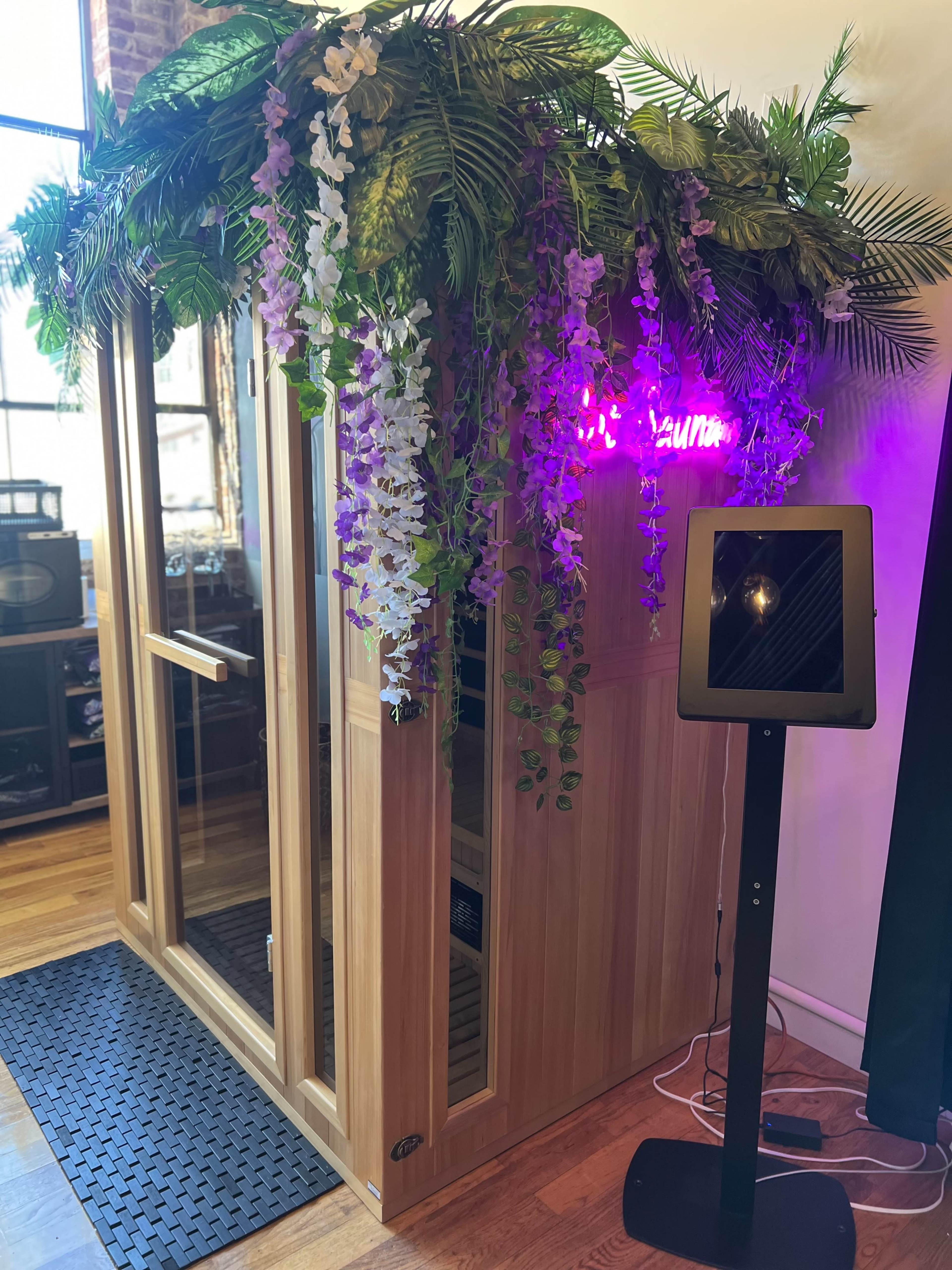 A wooden sauna with a floral decoration on top and a tablet stand beside it.