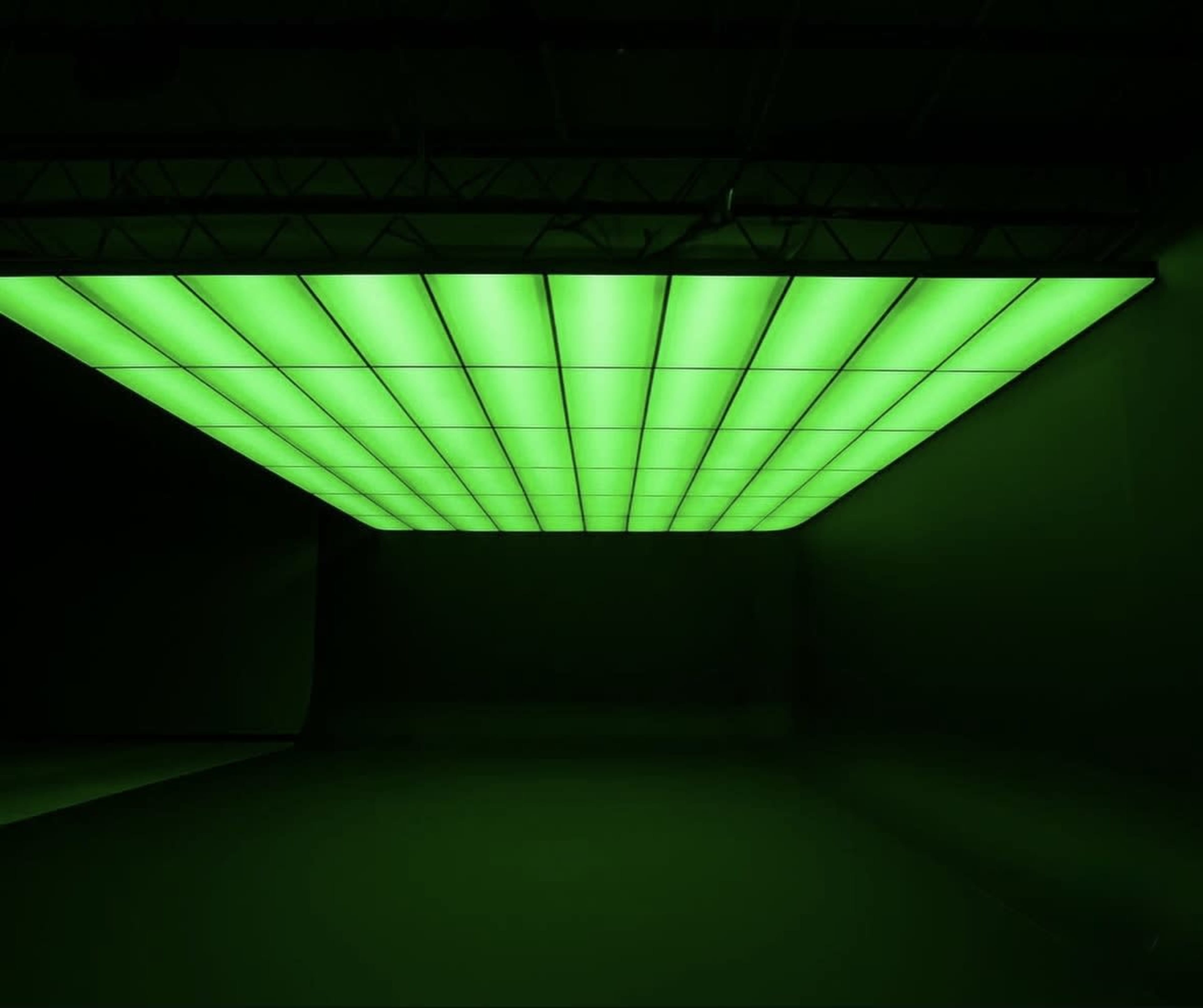 The image features a large ceiling panel illuminated with bright green light in a darkened space.