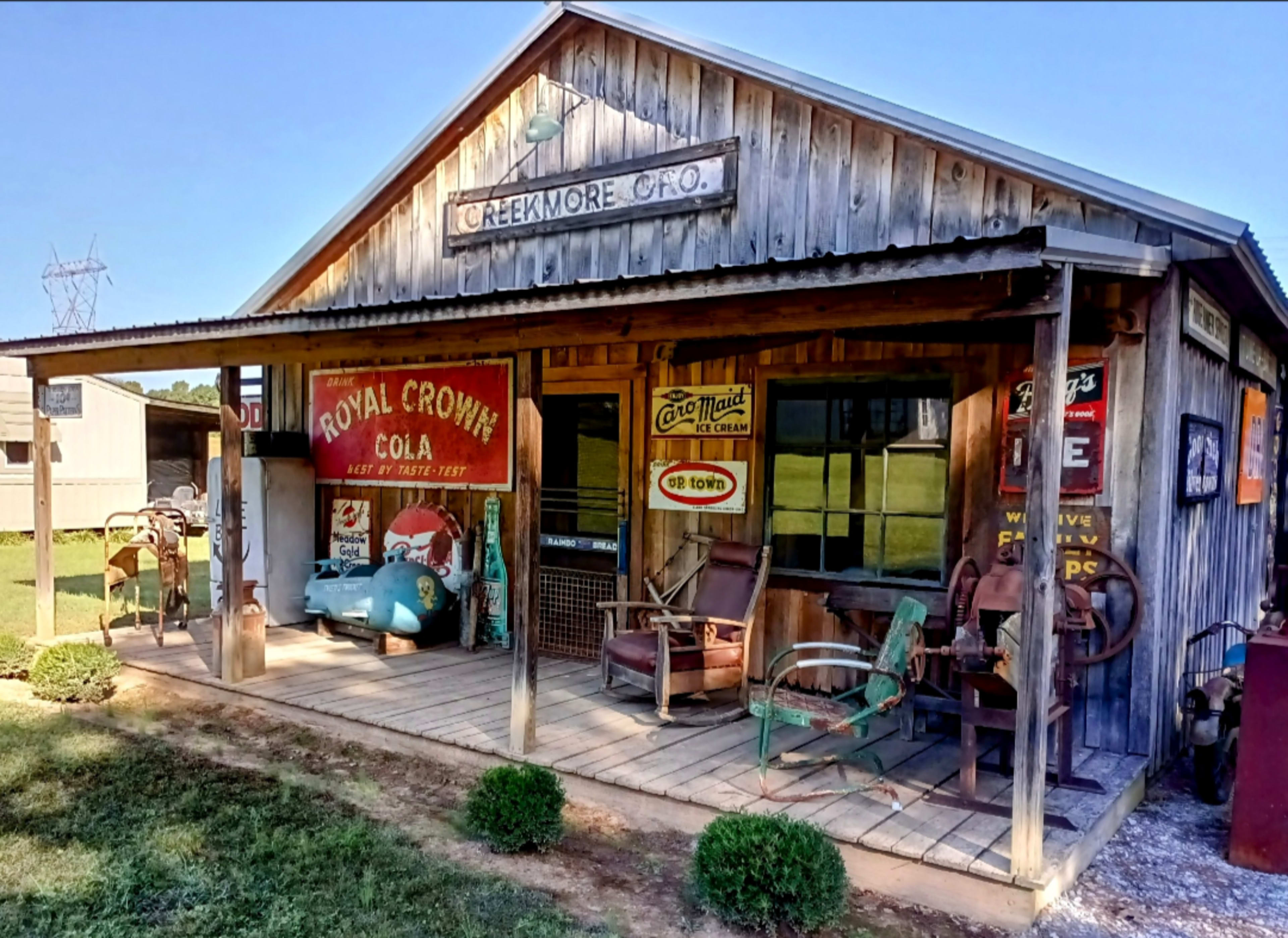 The image shows a vintage wooden storefront decorated with old advertisements, featuring an outdoor seating area and various nostalgic items.