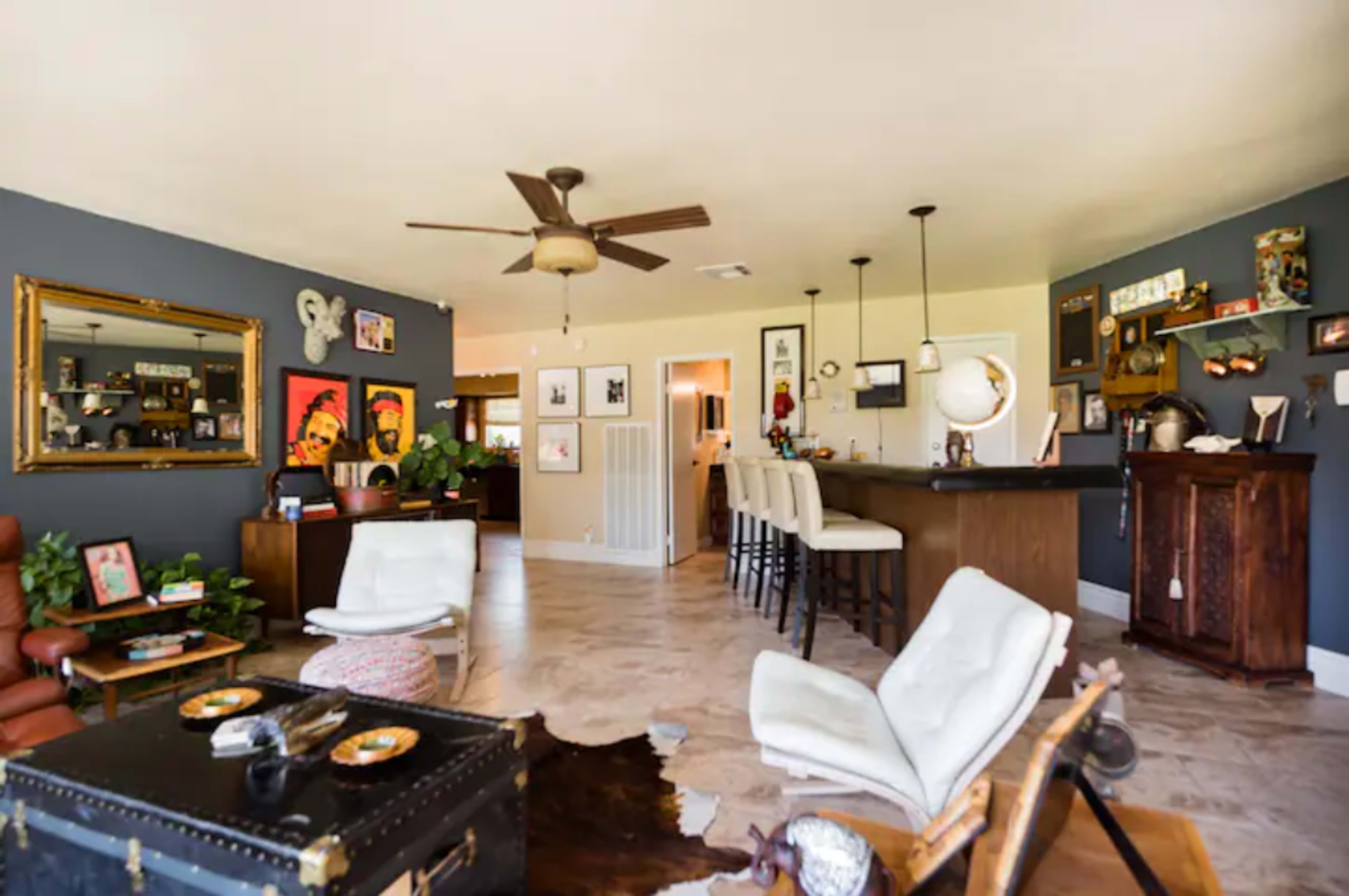 A spacious living area with a combination of seating, a bar, and decorative wall art, featuring a mix of modern and vintage furnishings.