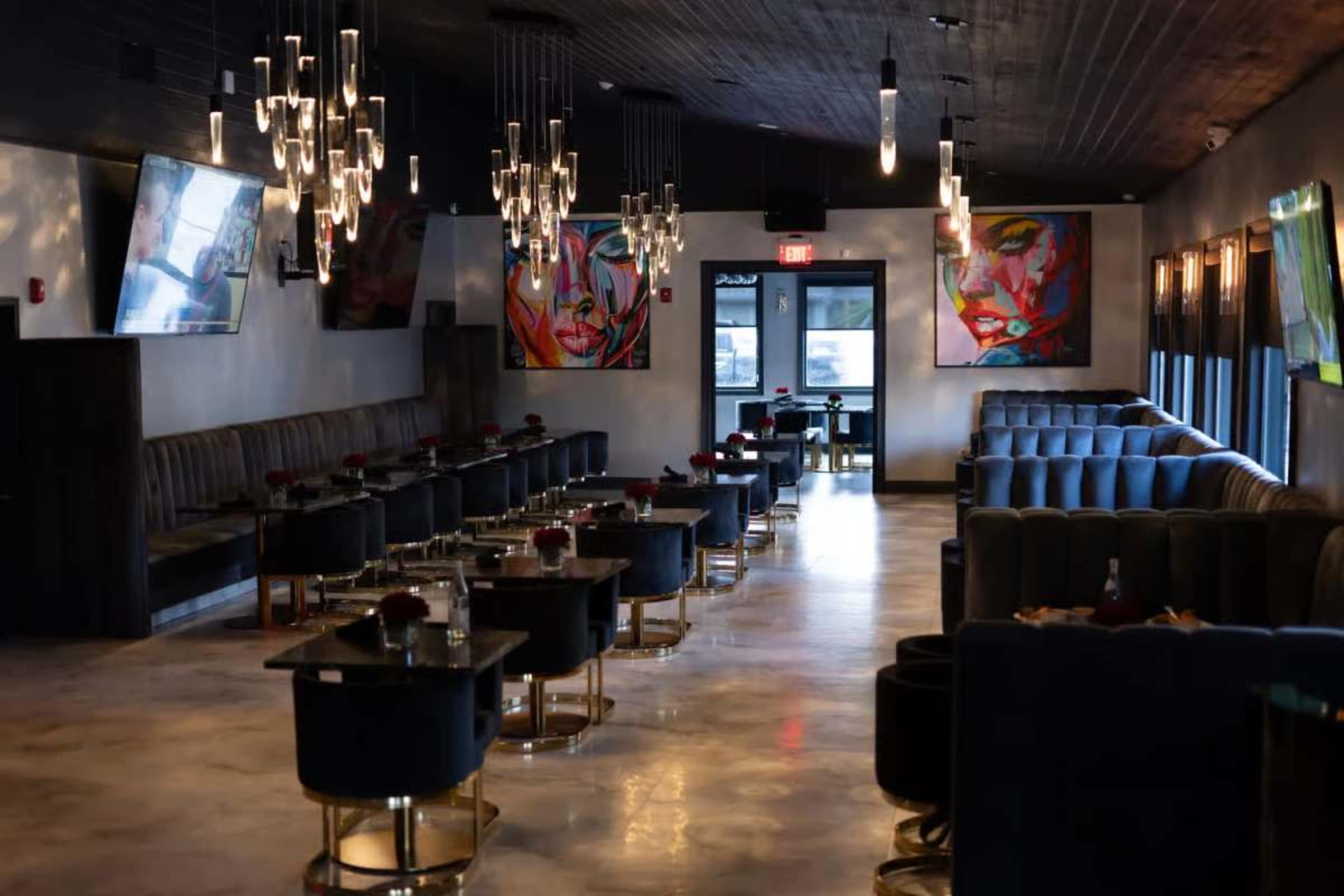 The image shows an upscale restaurant interior with modern lighting, dark seating, and colorful artworks on the walls.