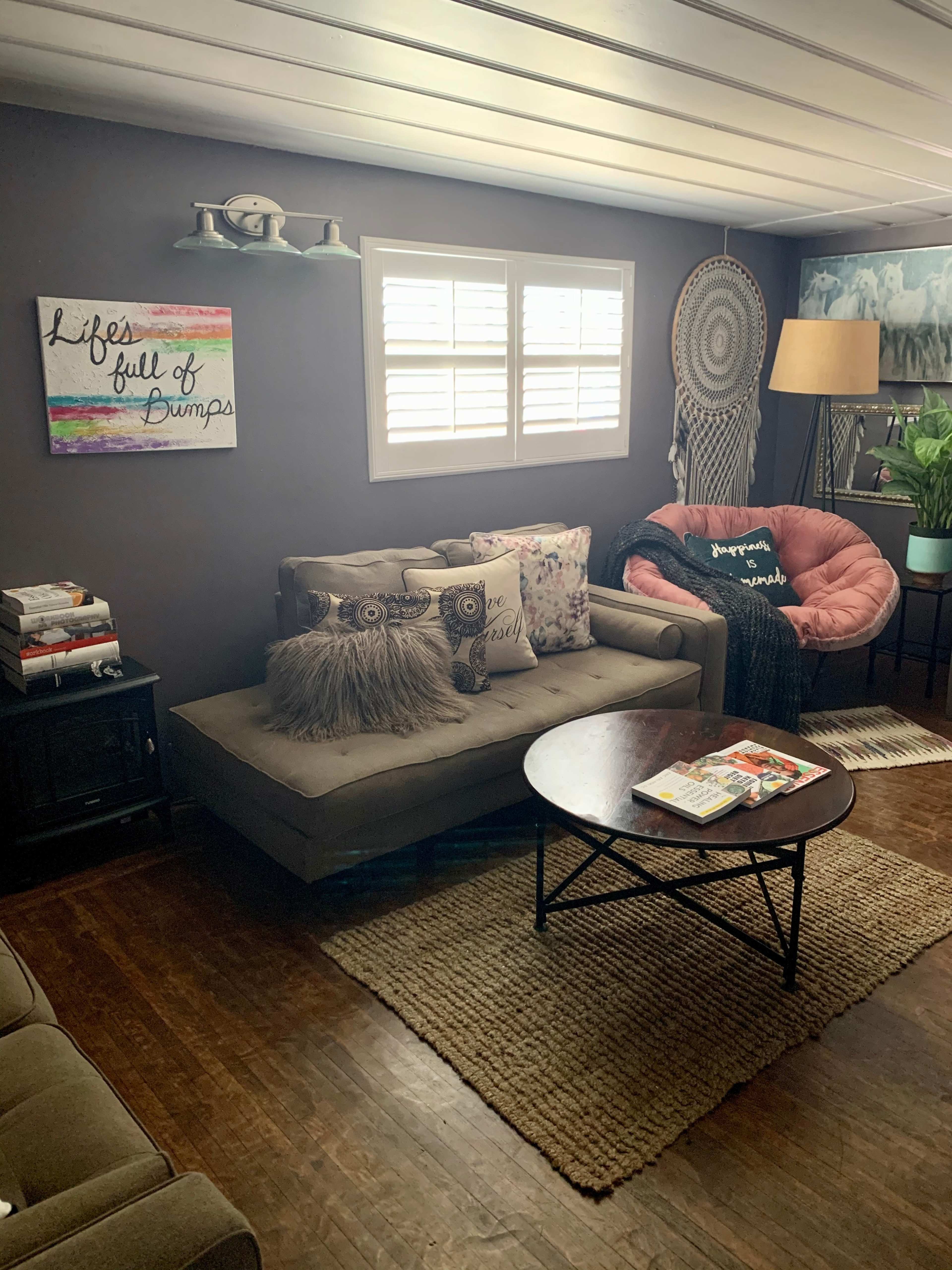 A well-furnished living room with a sofa, a round coffee table, and decorative pillows, featuring artwork on the walls and a lamp beside a pink chair.