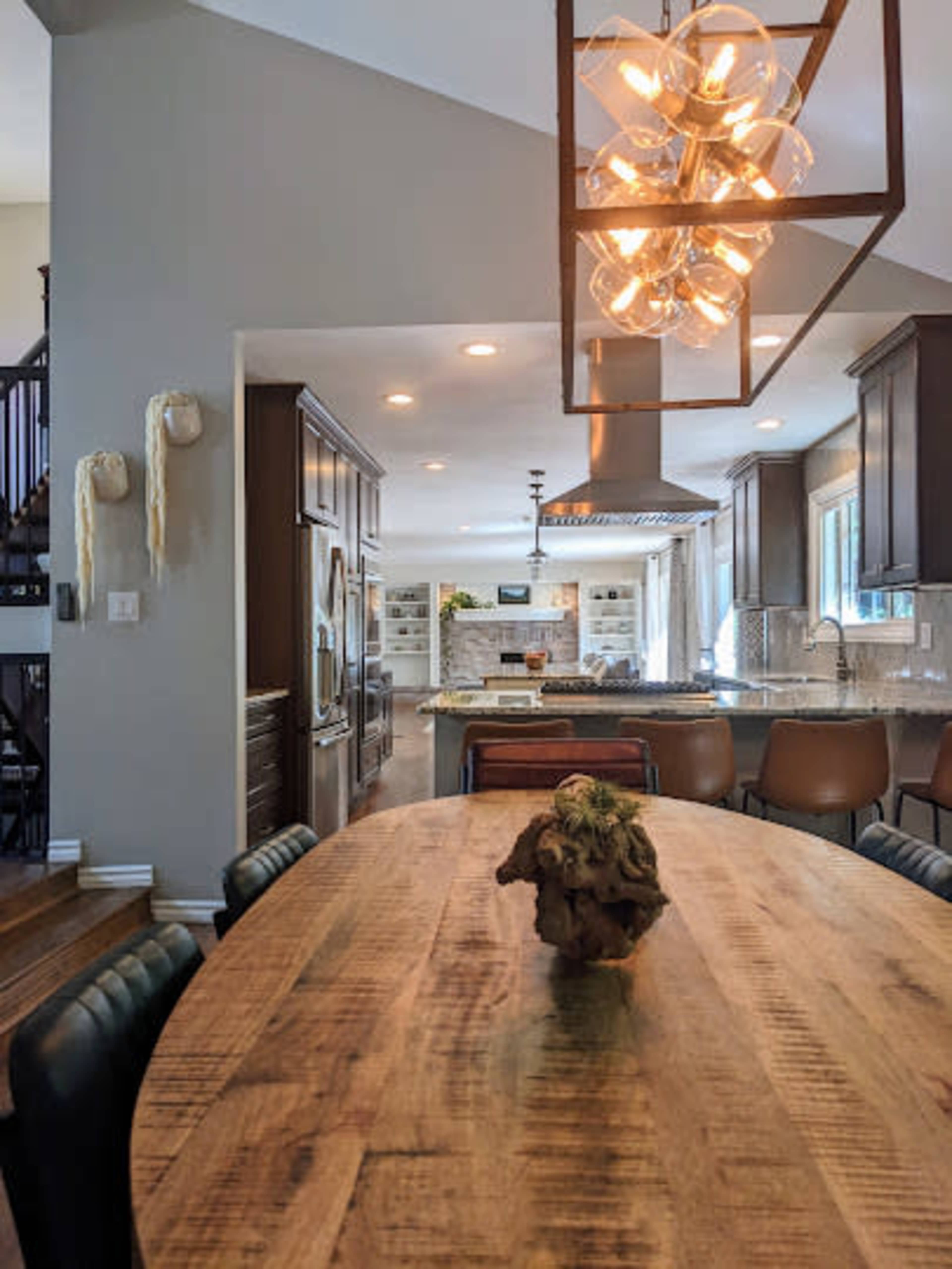 A spacious kitchen features a wooden dining table with a centerpiece, modern light fixtures, and sleek cabinetry.