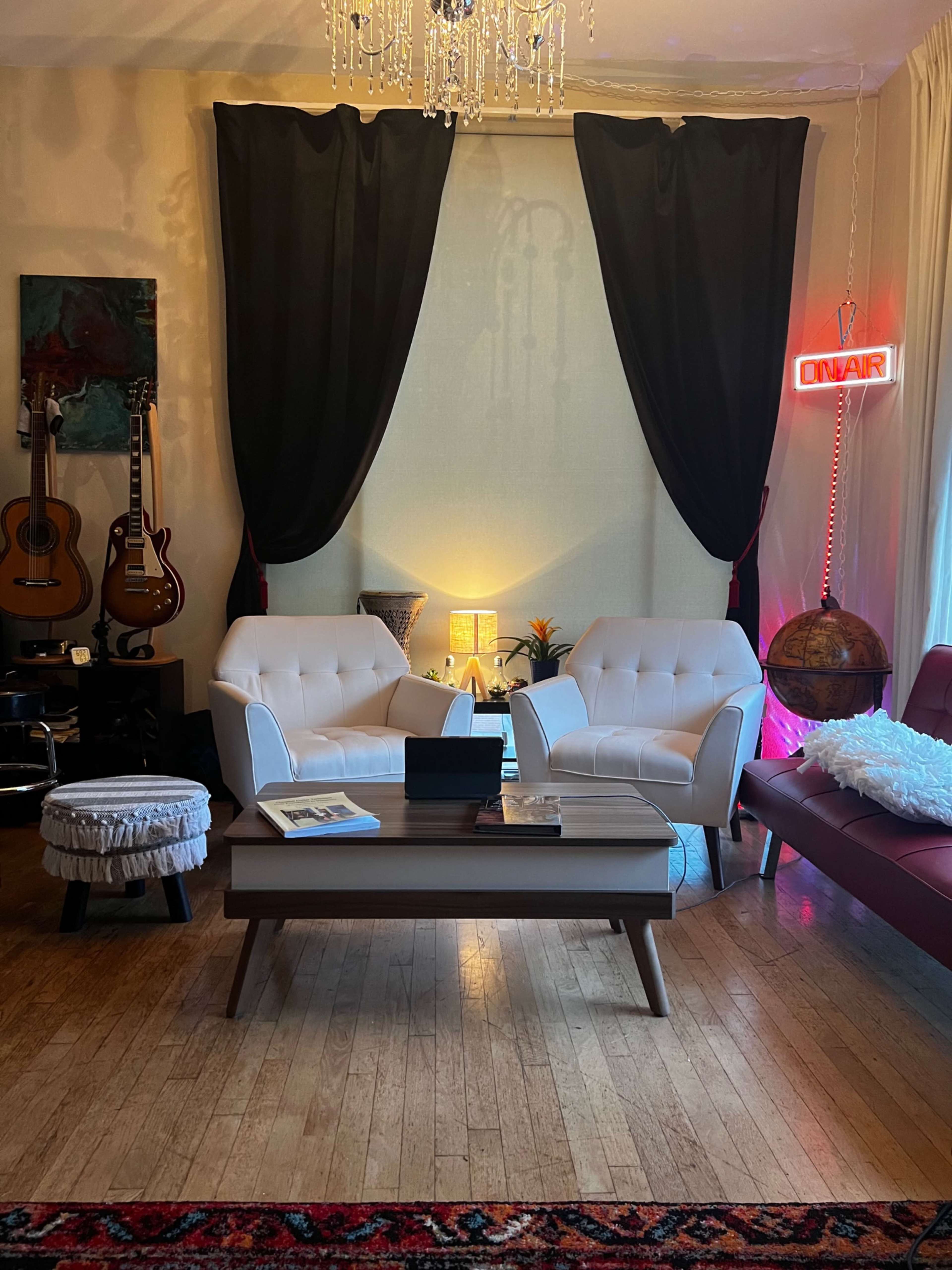 The image shows a living room with two white armchairs facing a wooden coffee table, a globe, guitars on the wall, and a neon "ON AIR" sign.