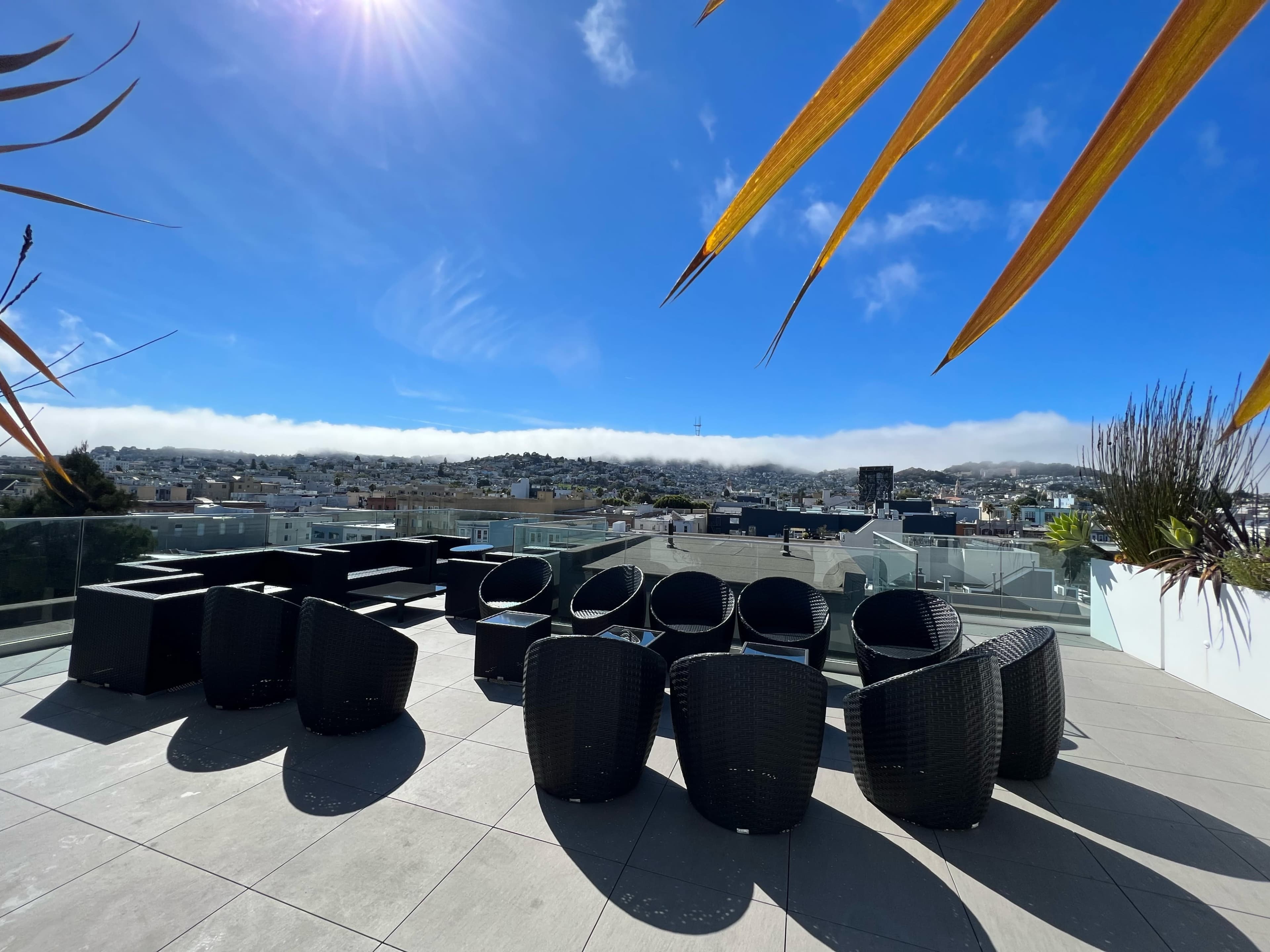 A rooftop terrace with black wicker furniture set against a clear blue sky and distant rolling hills.