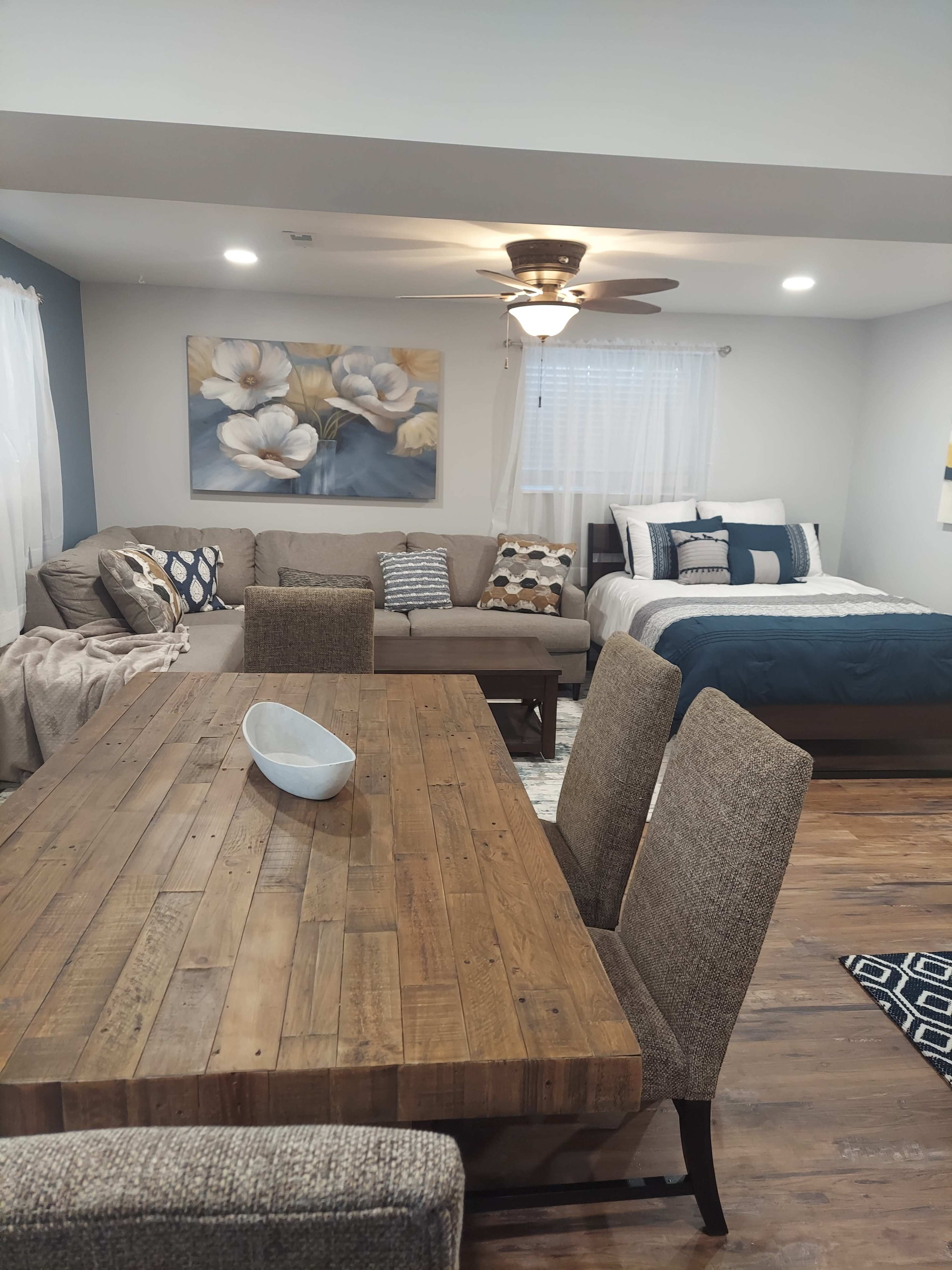 A cozy, combined living and sleeping area featuring a sectional sofa, a dining table, and a bed with blue and white bedding.