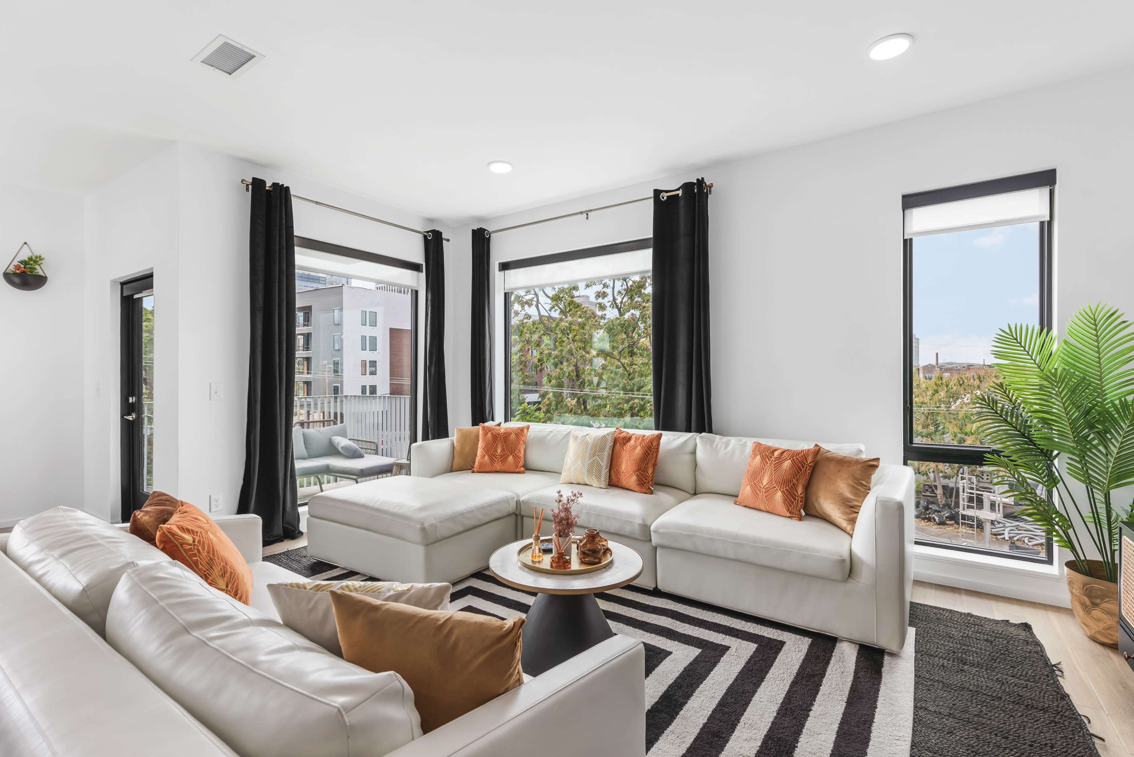 The image showcases a modern living room with a sectional sofa, a round coffee table, and large windows that provide a view of an outdoor area.