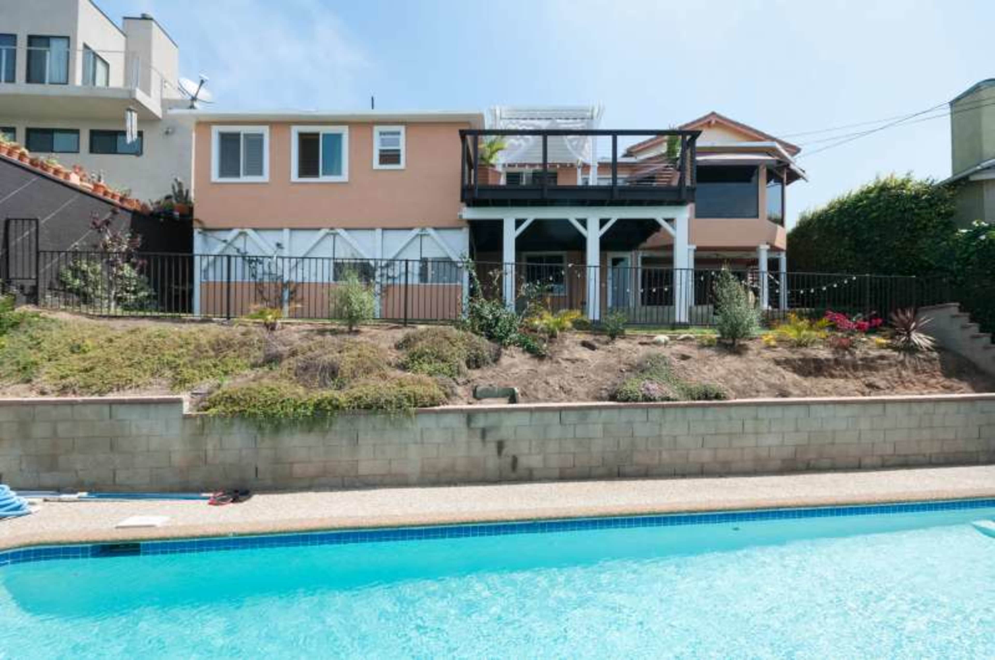 A two-story house with a deck overlooks a swimming pool, surrounded by a landscaped yard.