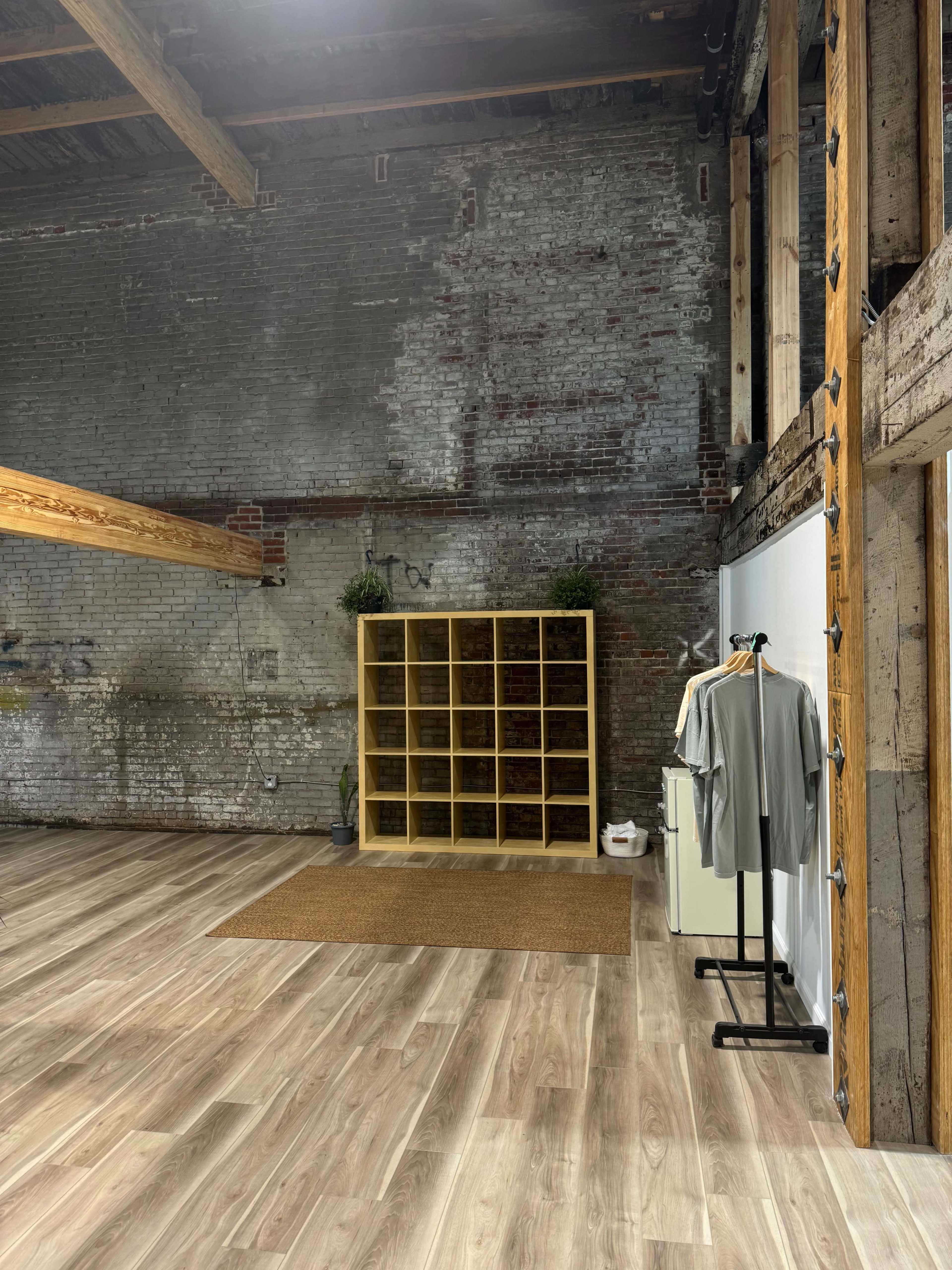An industrial-style interior with exposed brick walls, wooden beams, a shelving unit, and a clothing rack.