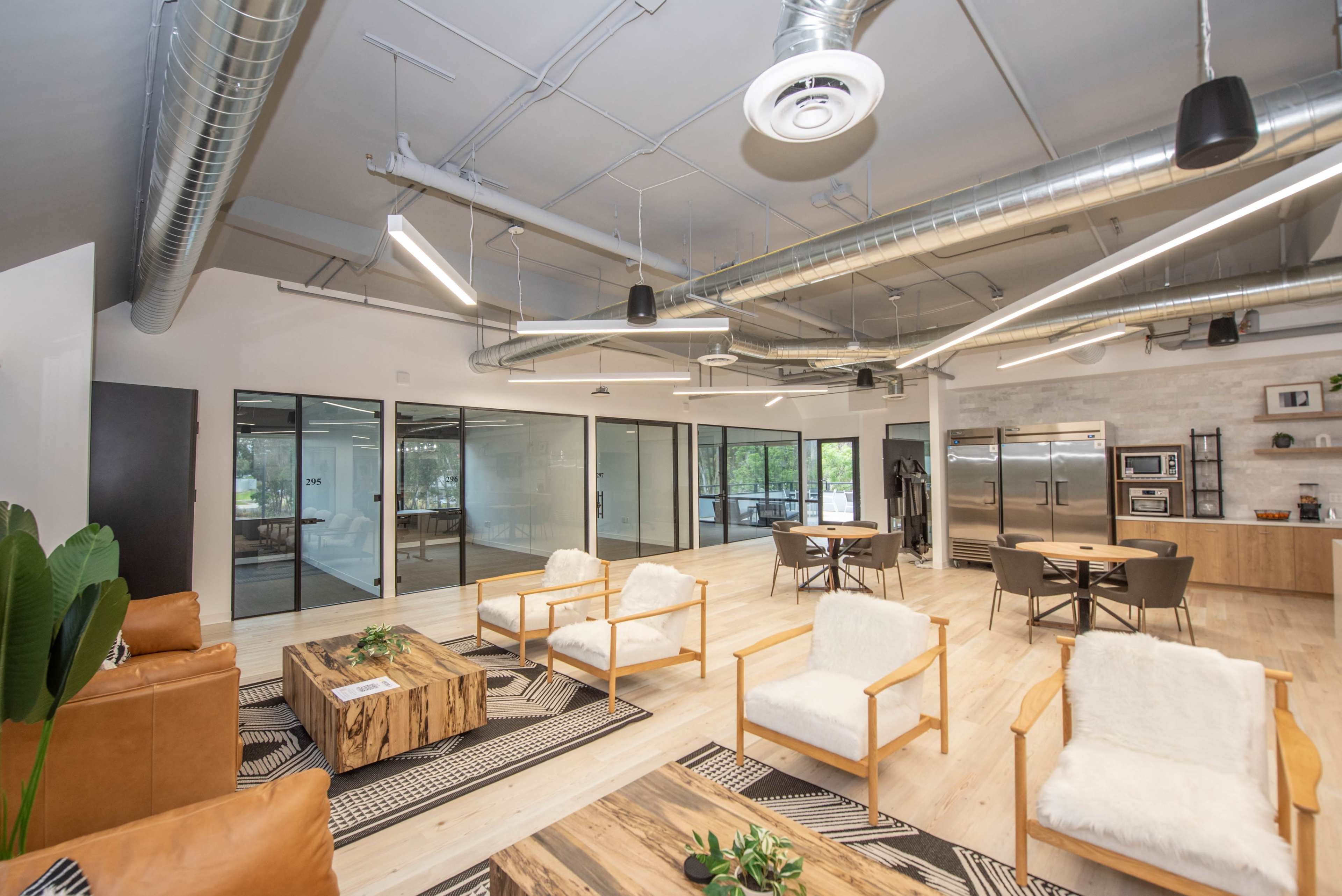A modern office space with wooden furniture, open seating areas, and large glass windows.