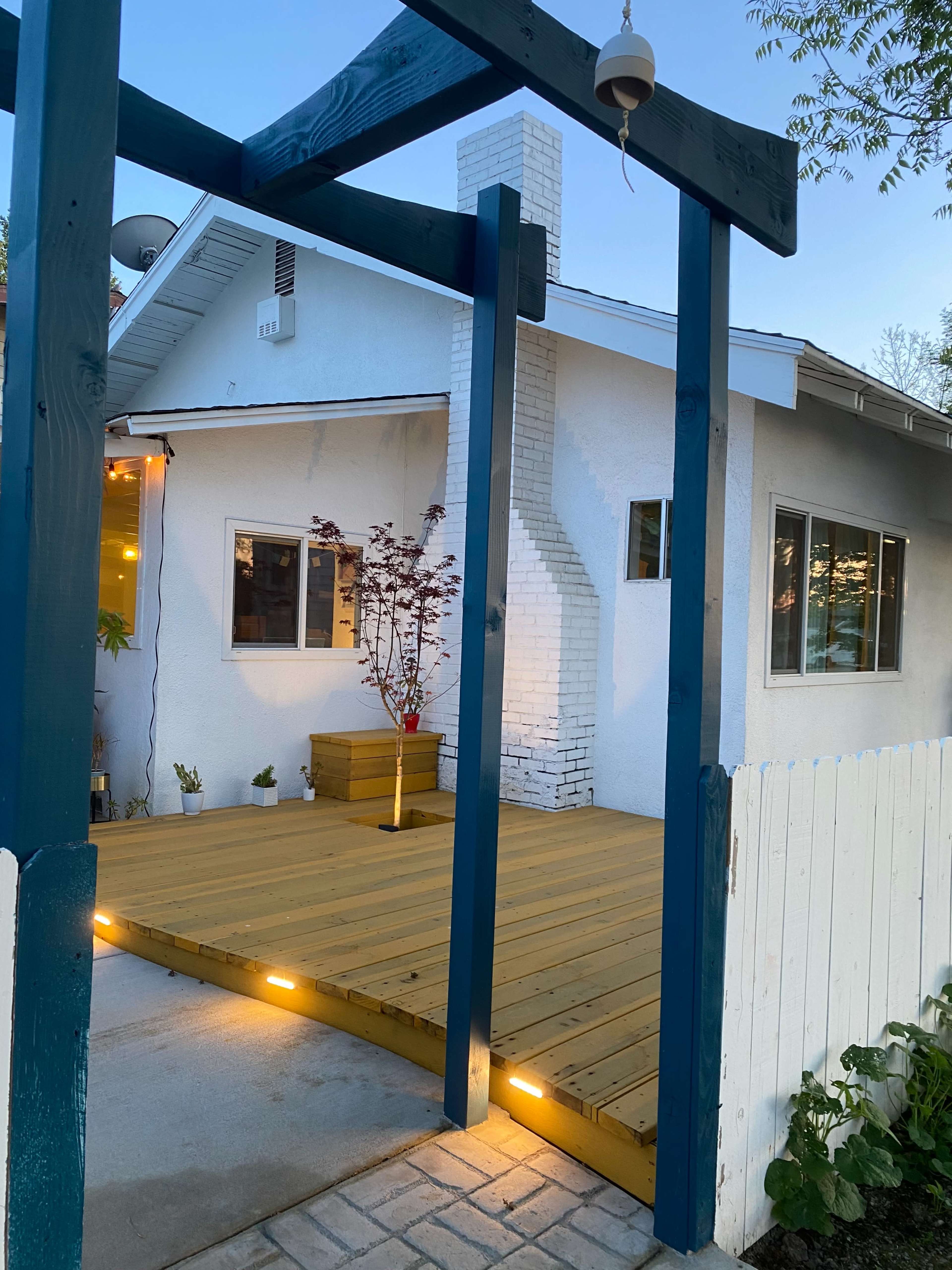 A wooden deck attached to a house, featuring a blue wooden archway and a white fence in the foreground.