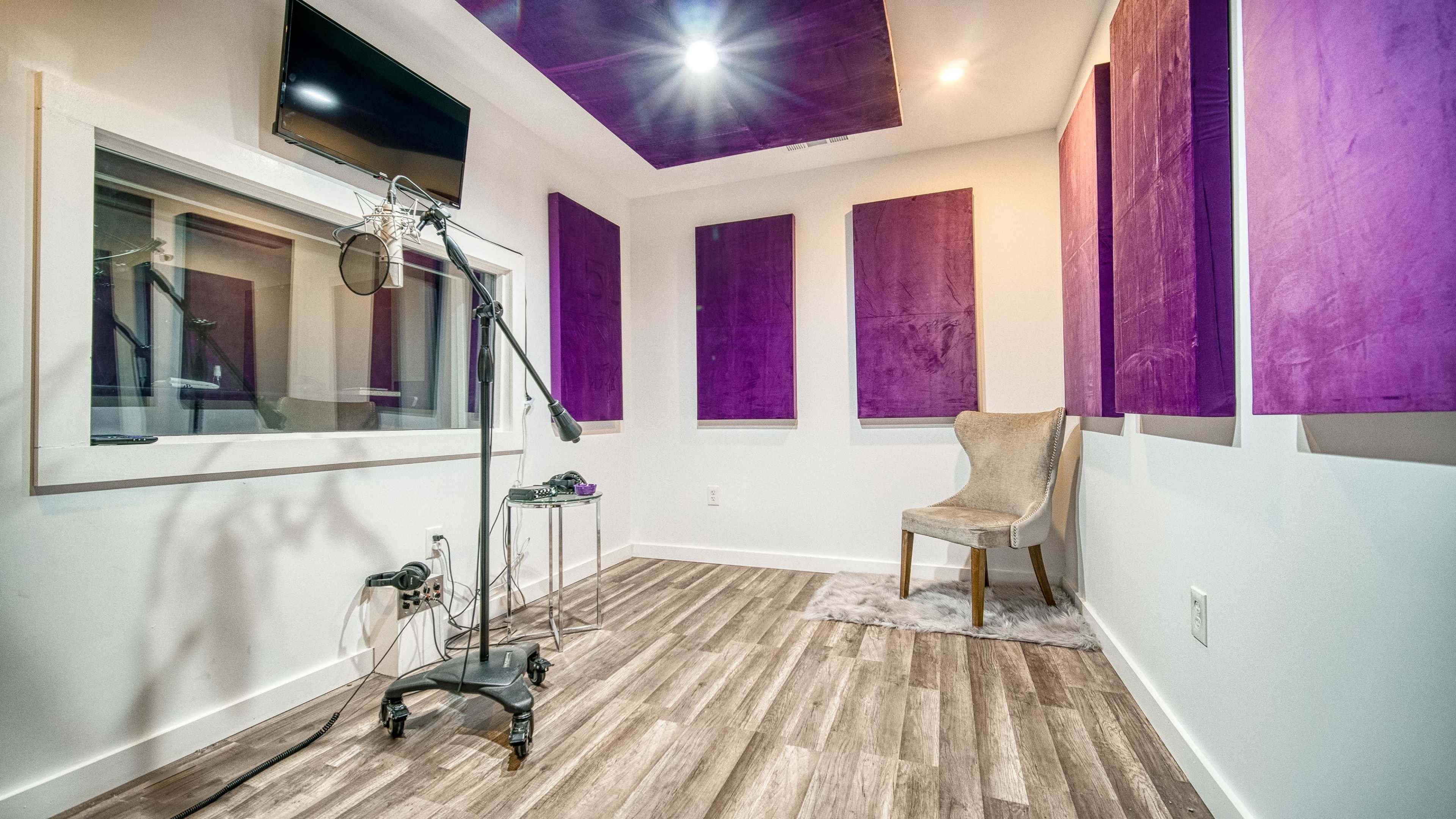 A vocal recording booth with a microphone stand, a chair, and soundproof panels on the walls.