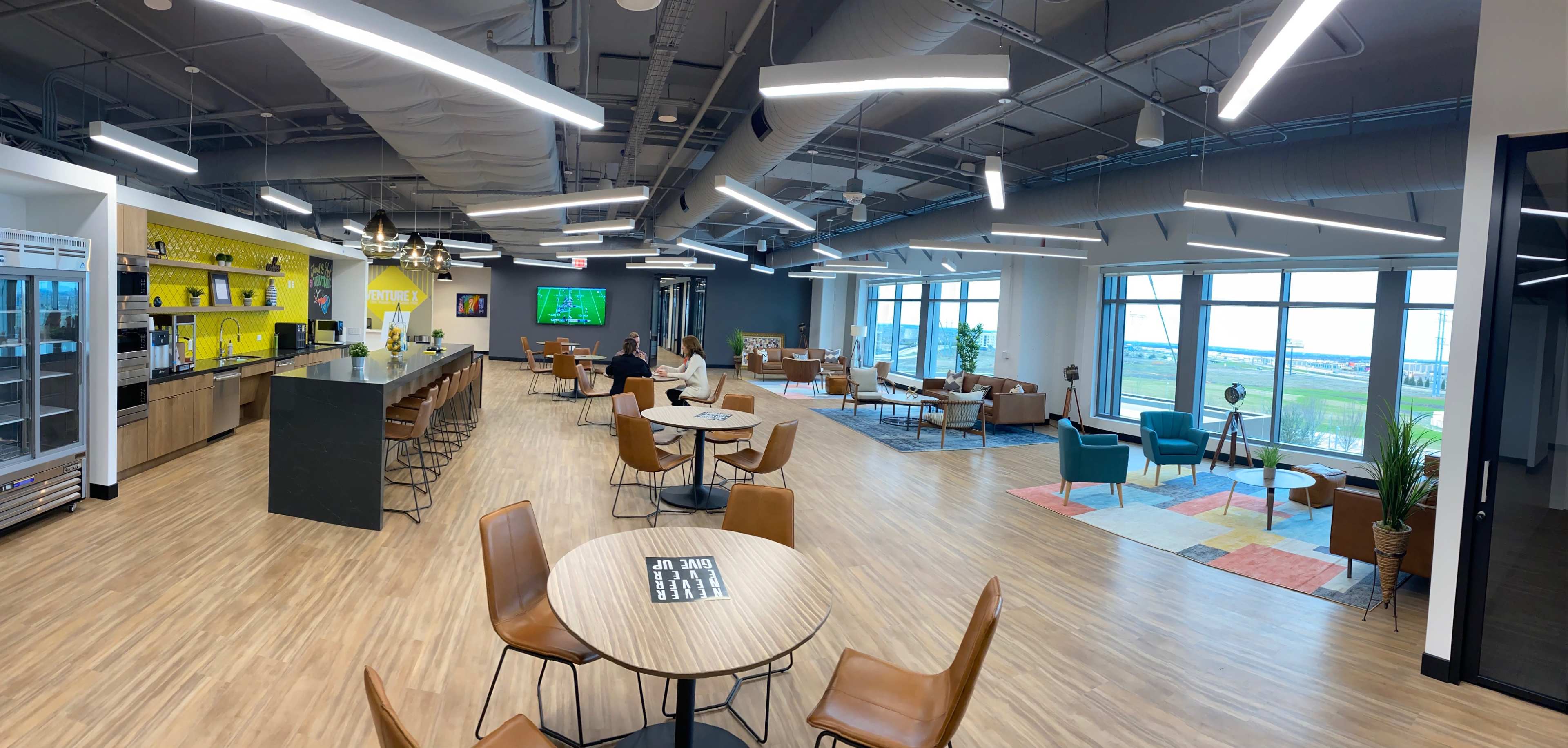 A modern office lounge area with seating arrangements, a bar counter, and large windows showcasing the outside view.