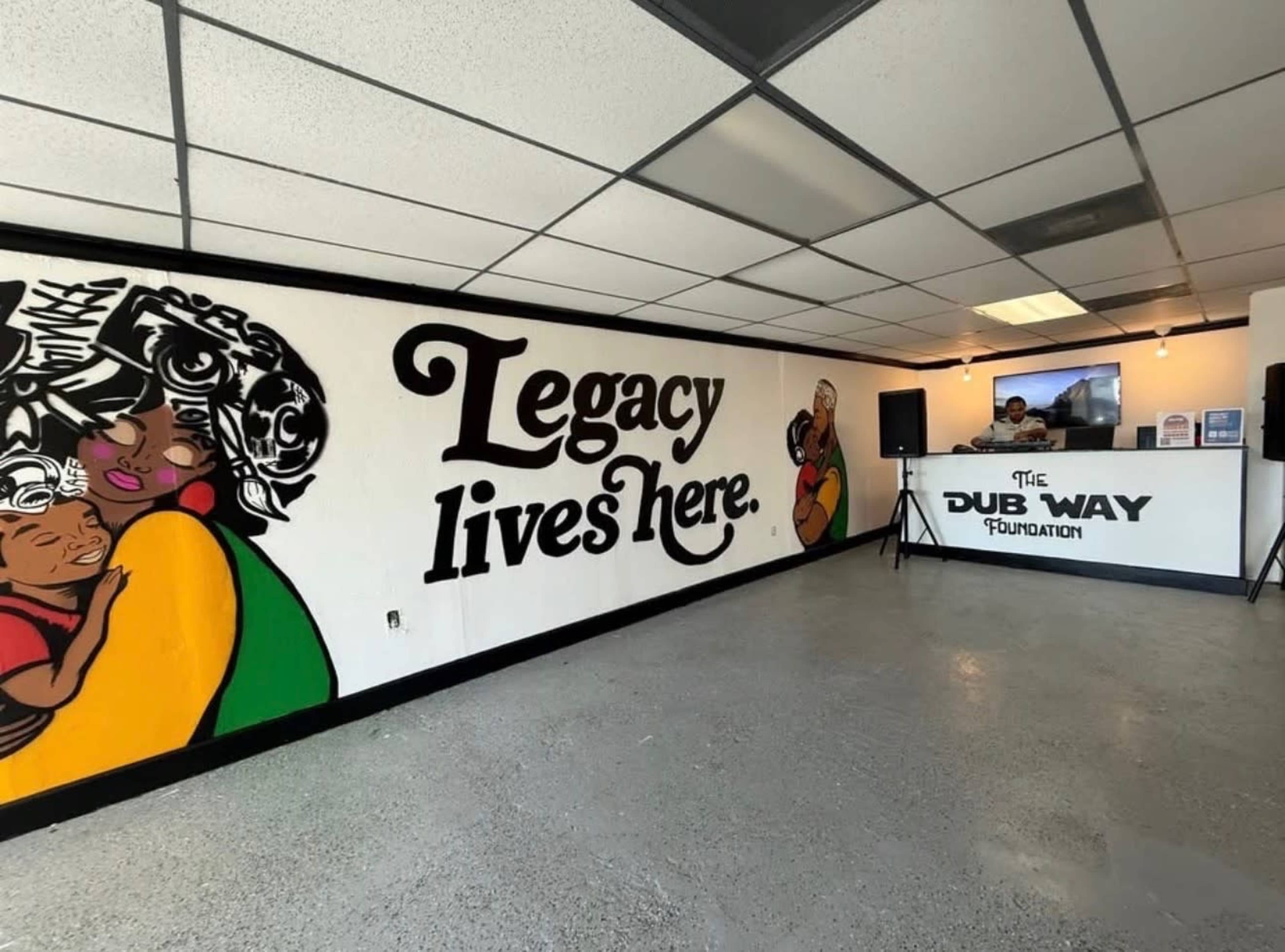 The image shows an interior space featuring a mural with the text "Legacy lives here" on one wall and a reception area with a counter labeled "THE DUB WAY FOUNDATION."
