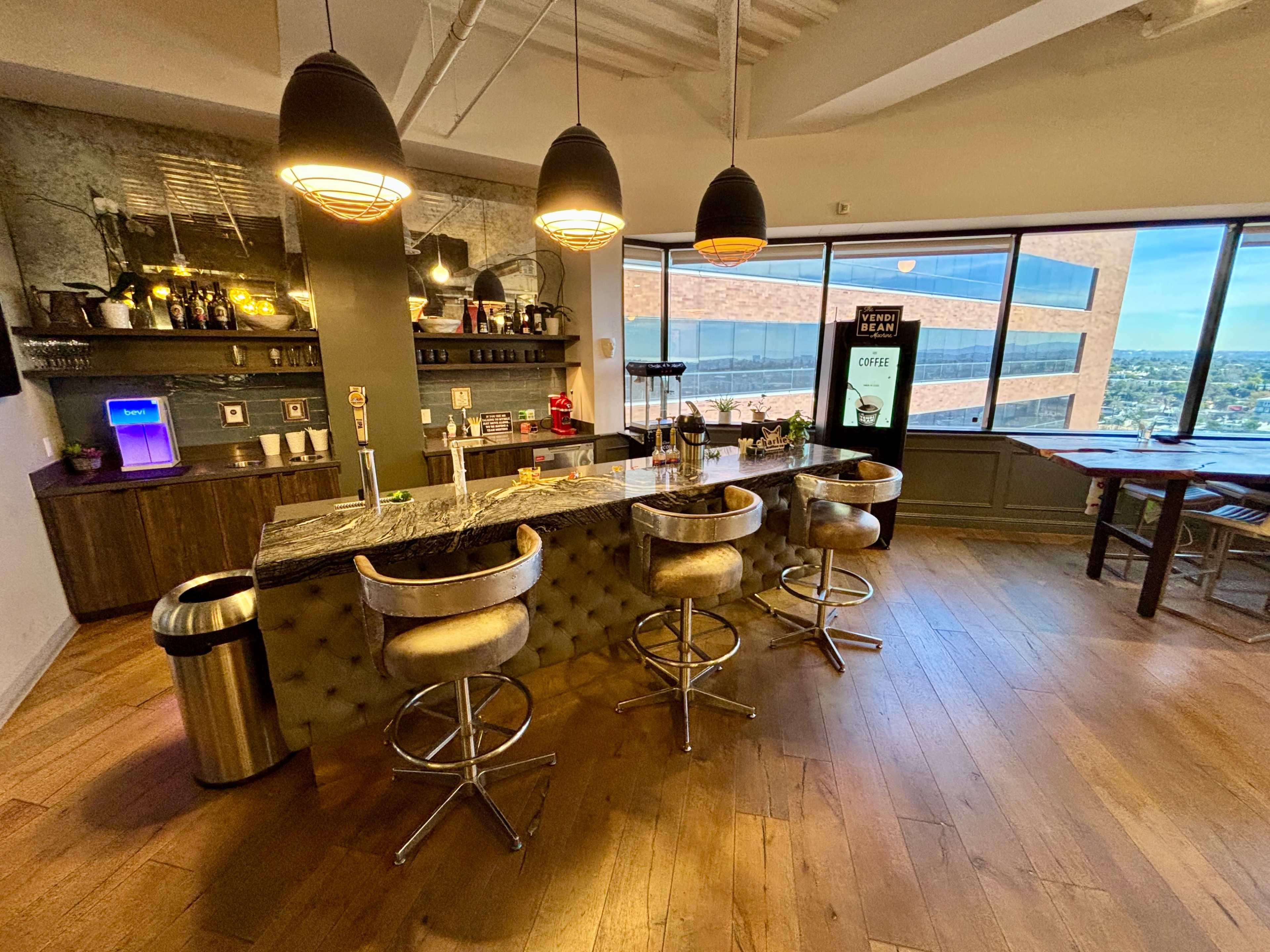 A modern bar area features a marble countertop, three upholstered stools, and a large window showing a city view.
