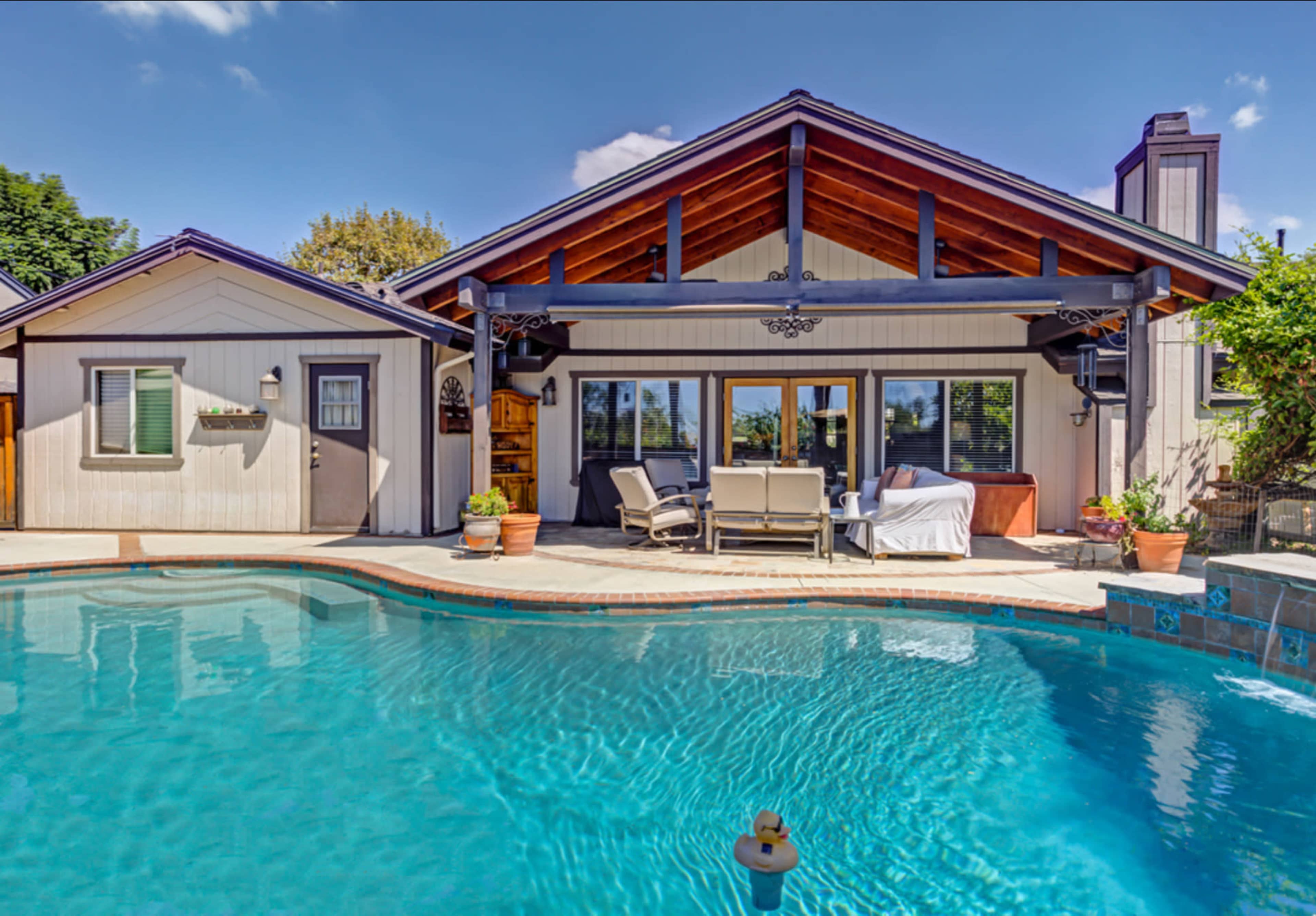 A modern home with a landscaped backyard features a swimming pool and outdoor seating area under a covered patio.