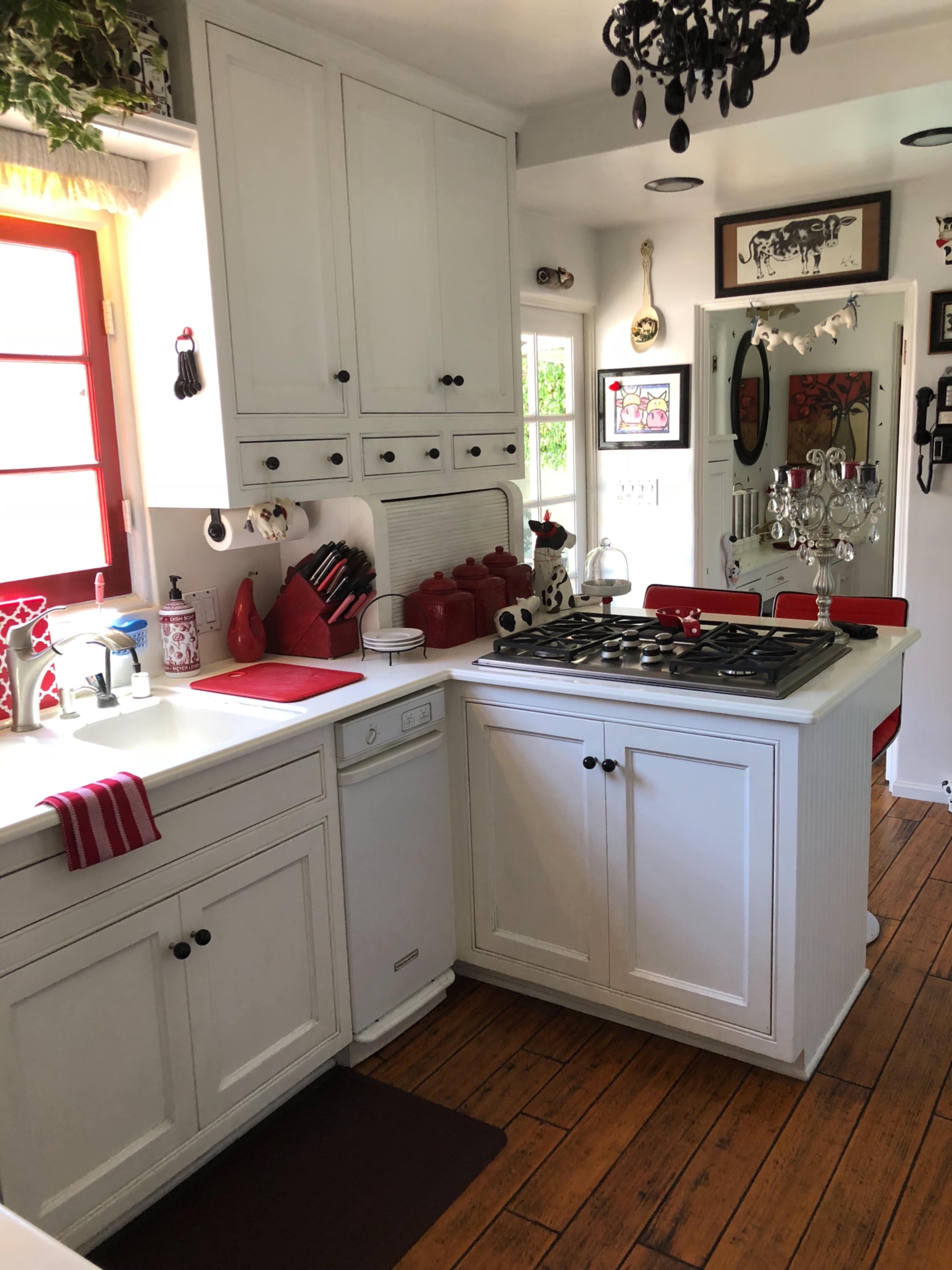 The kitchen features white cabinetry, a red accent wall, and a combination of modern and vintage decor with wooden flooring.