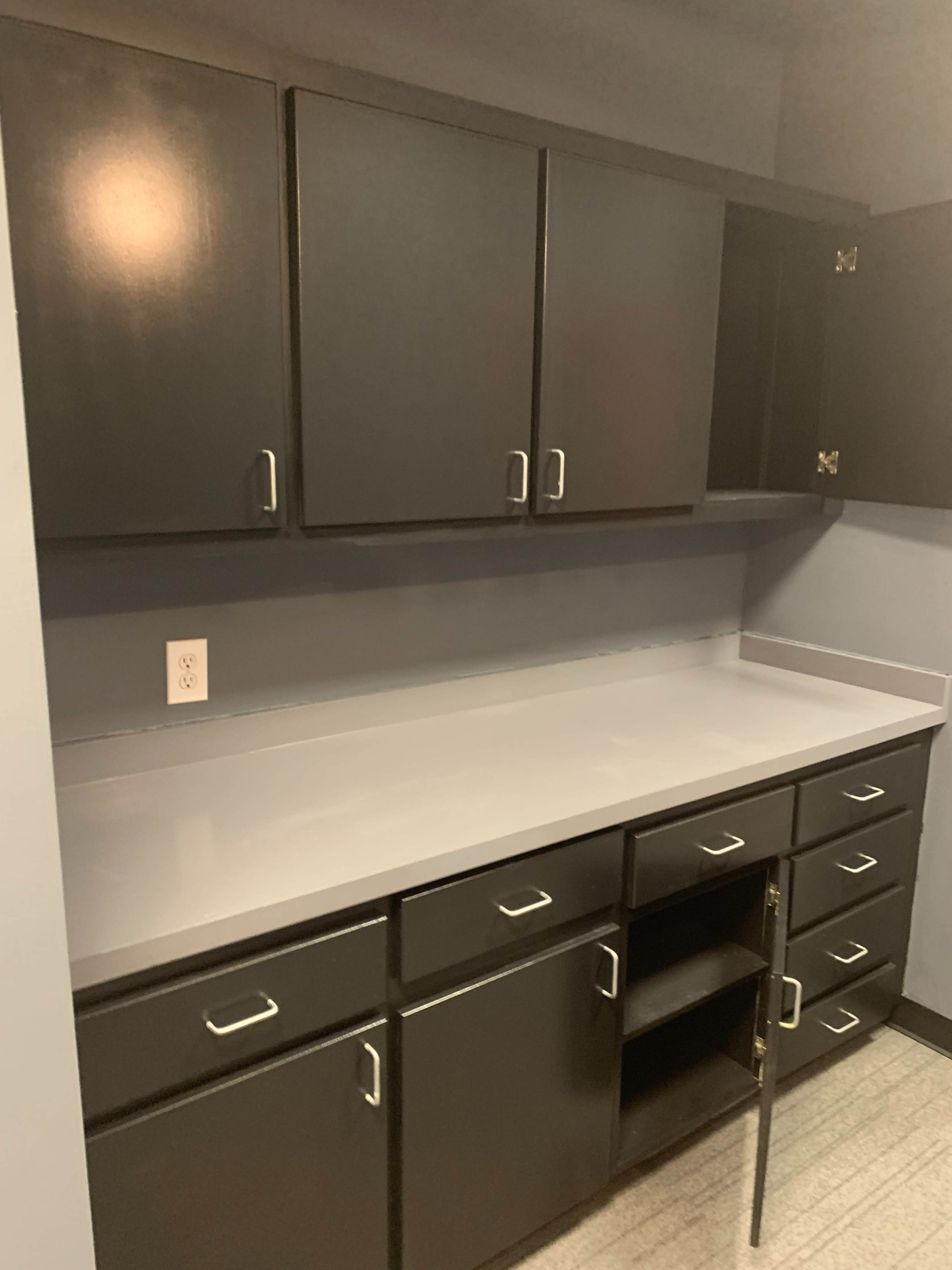 A kitchen space with dark cabinets above and below a gray countertop, featuring a central cabinet with an open space.