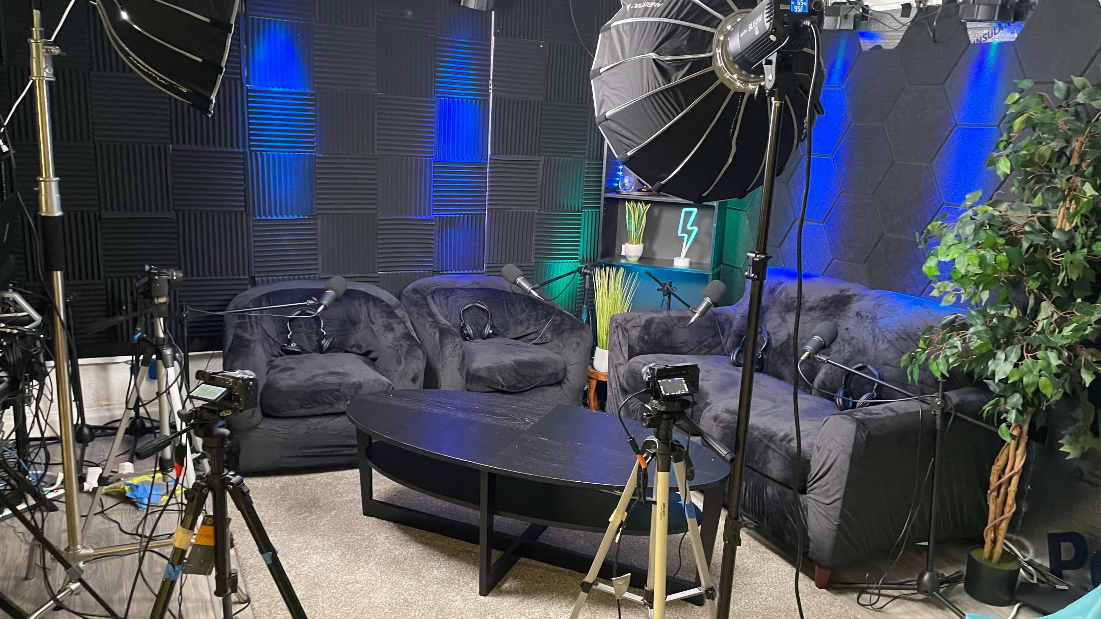 The image shows a recording studio setup with microphones, cameras, and black furniture arranged around a low table.