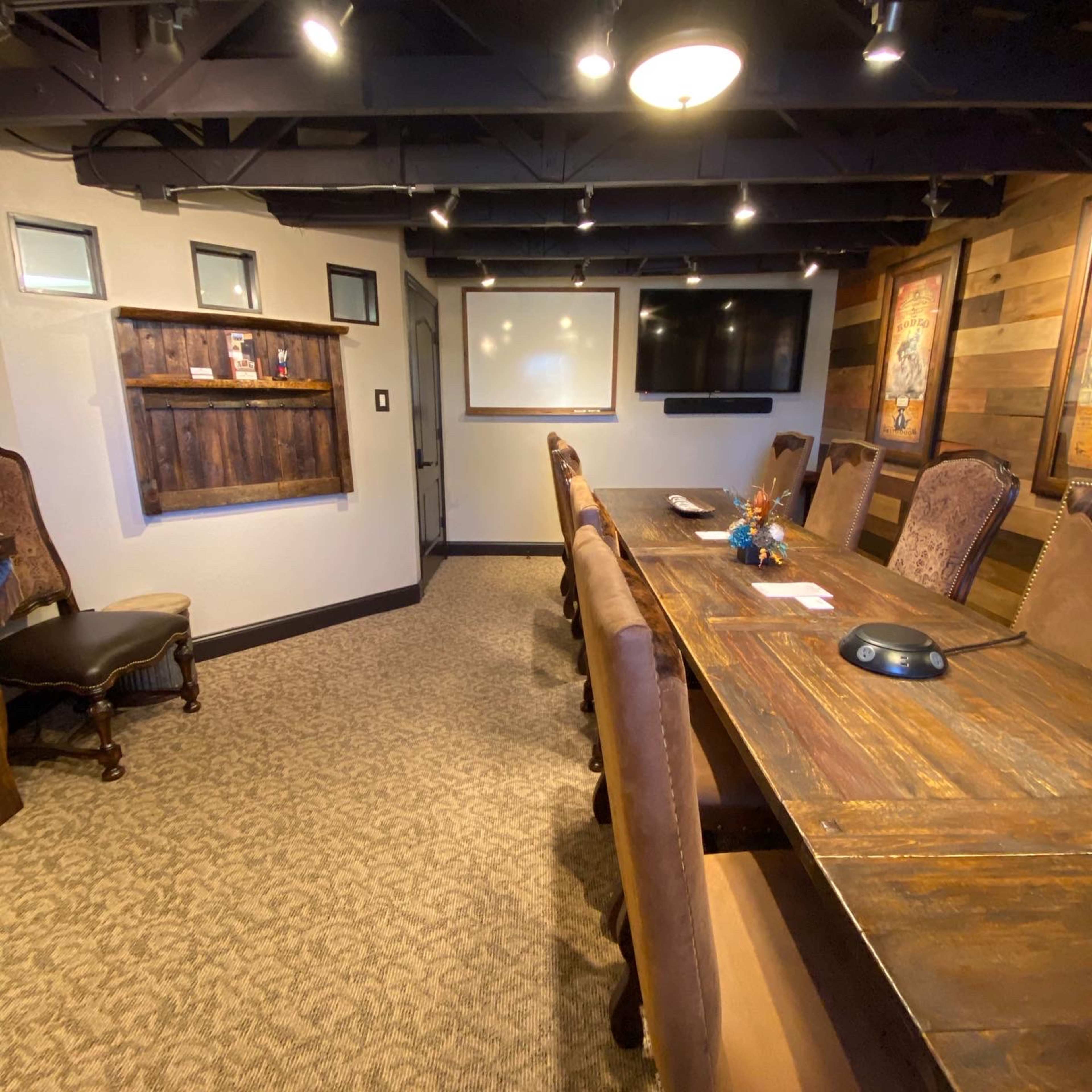 A conference room with a long wooden table, padded chairs, and a wall-mounted television.