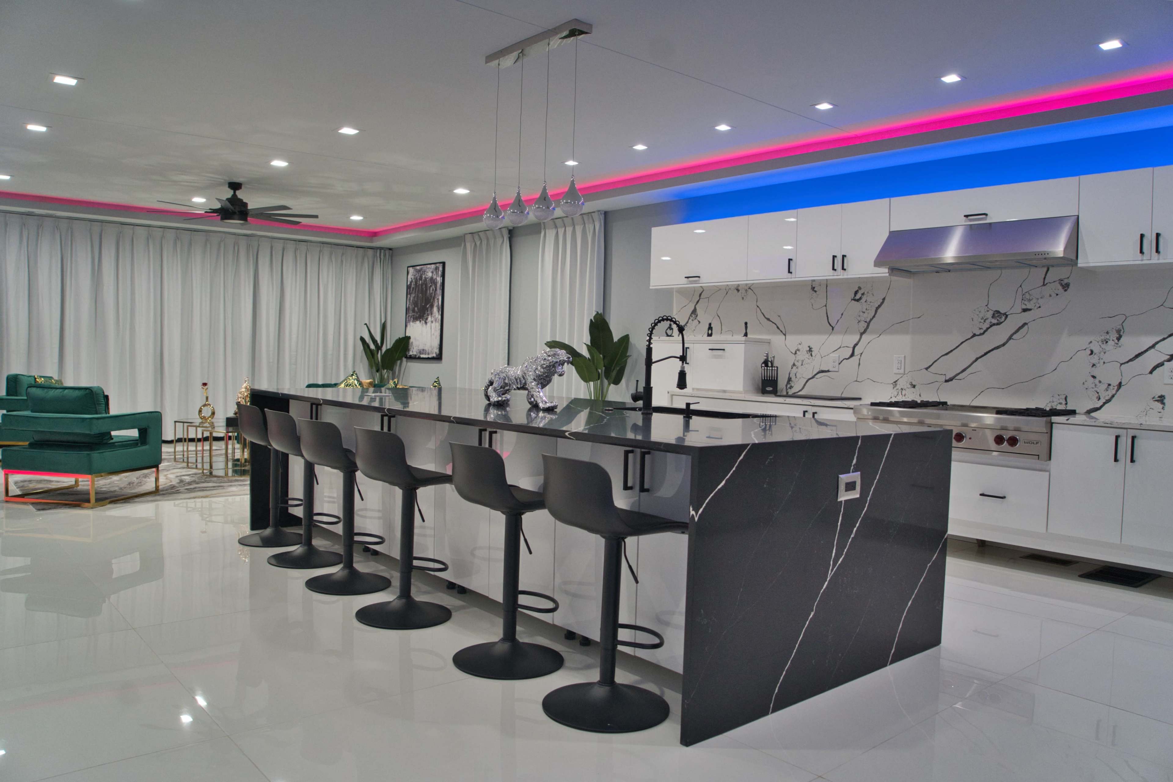 A modern kitchen featuring a sleek black and white marble island with high stools, illuminated by colorful LED lights along the ceiling.