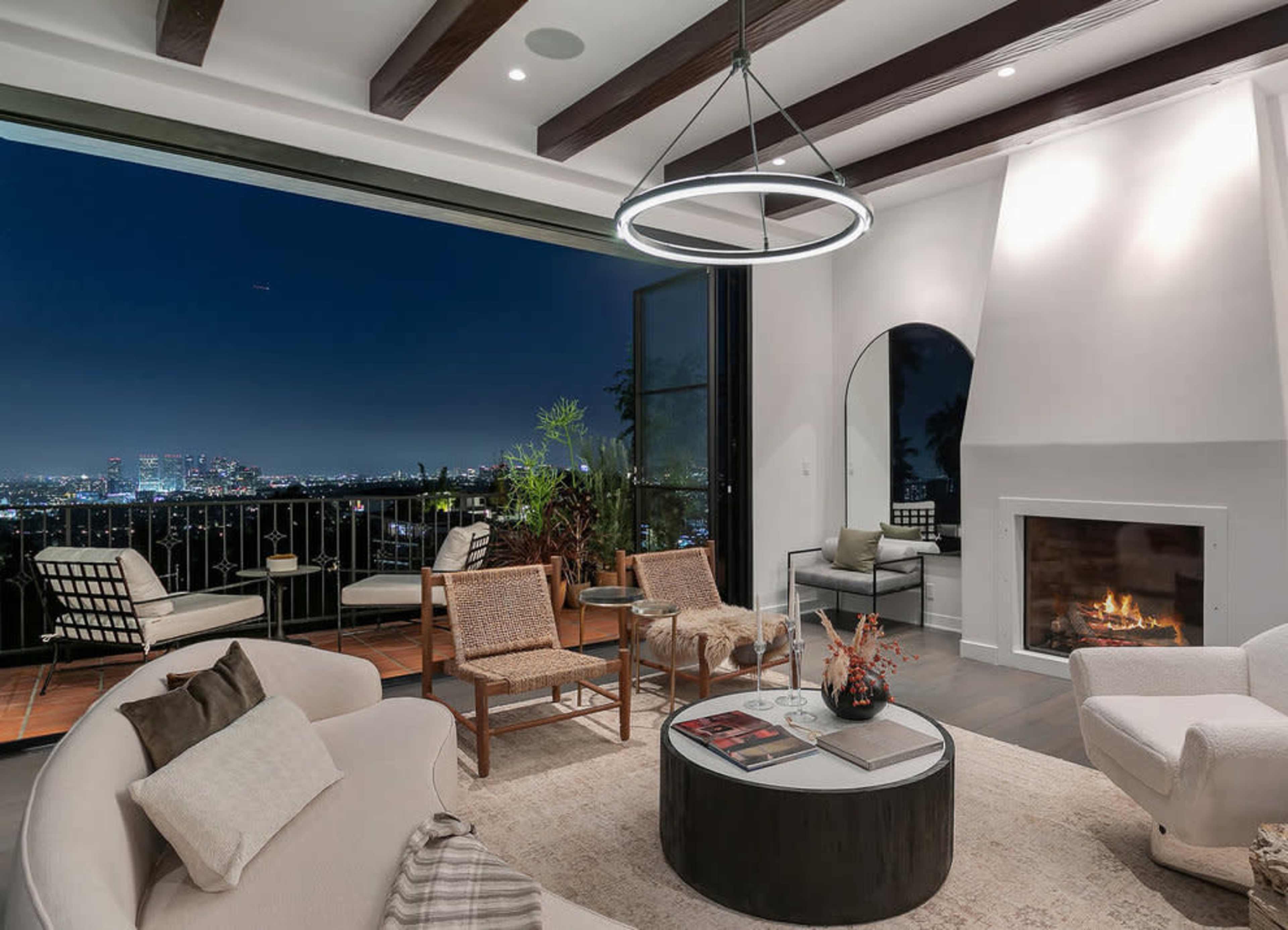 A modern living room features a circular coffee table, a fireplace, and large windows showcasing a city skyline at night.