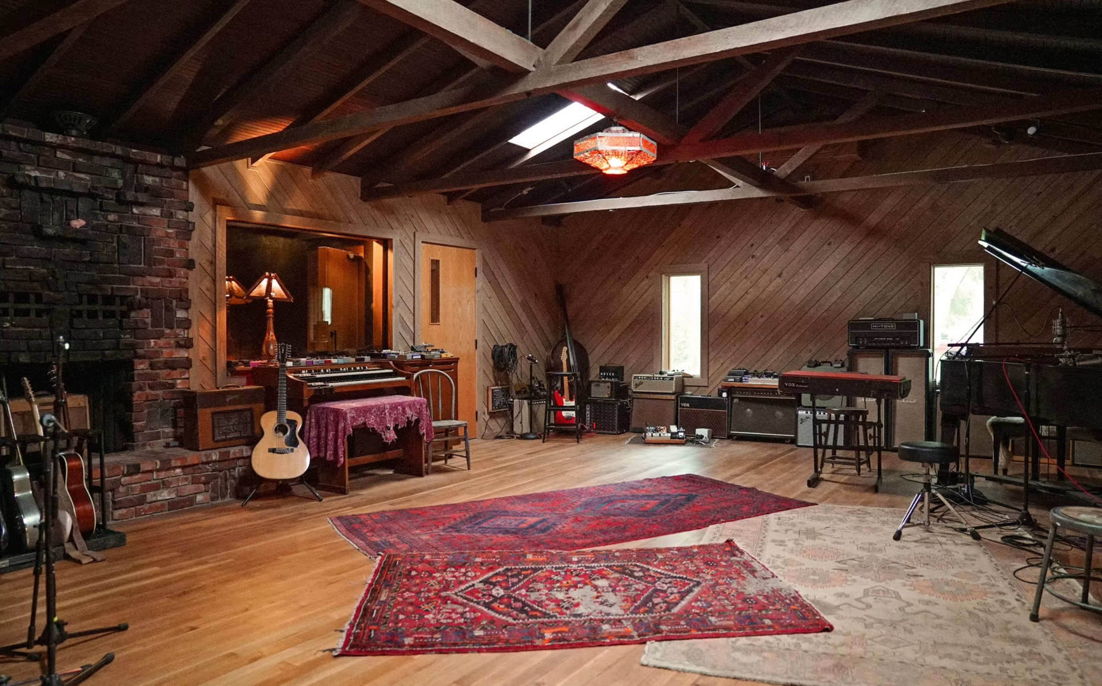 The image shows a wooden acoustic space with a brick fireplace, various musical instruments, and decorative rugs on the floor.