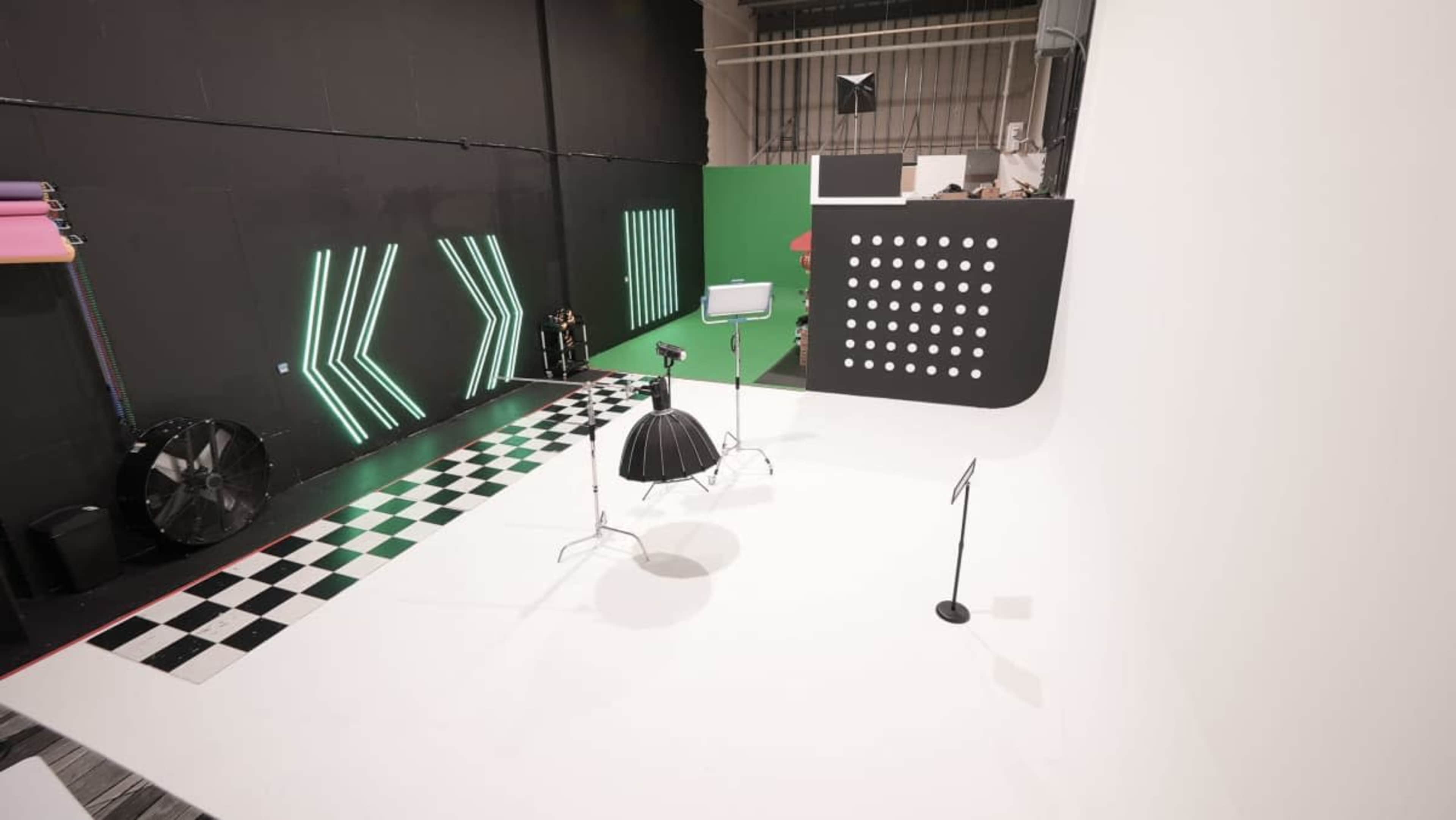 The image shows a photography studio with a checkered floor, colorful backgrounds, and lighting equipment arranged for a photoshoot.