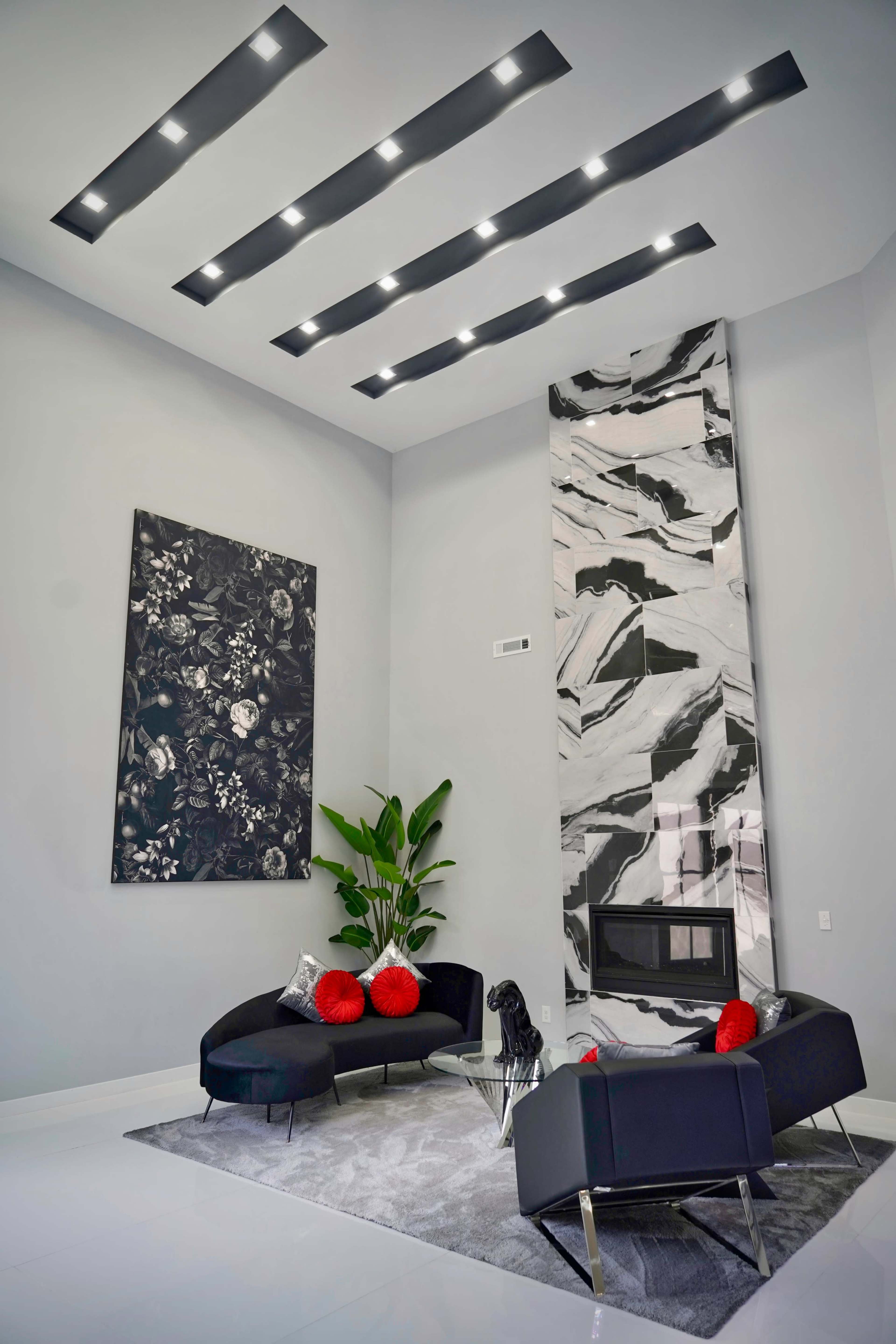 A modern living room with a sleek black sectional sofa, a marble wall featuring a fireplace, and a large abstract artwork on the wall.