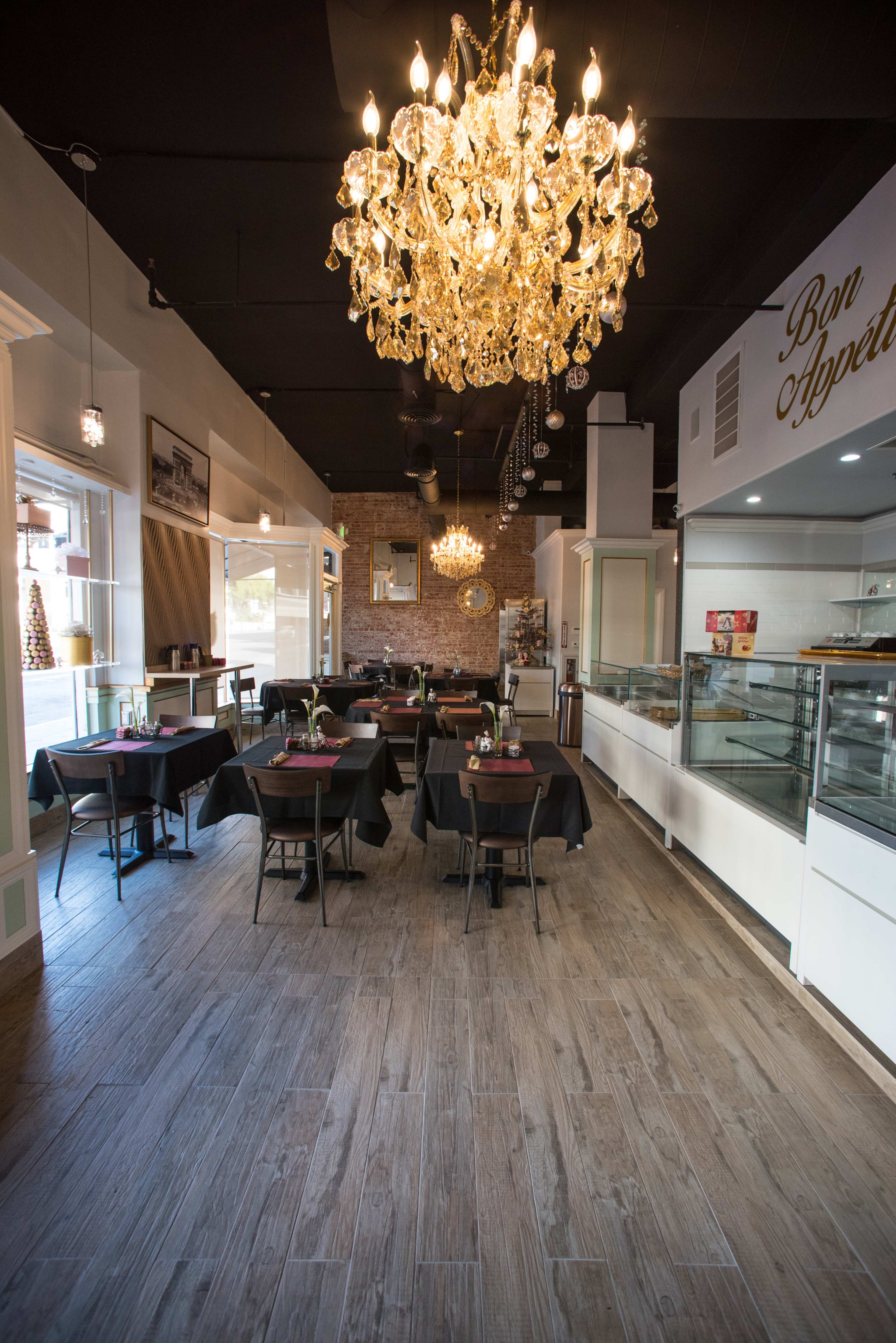 A well-lit restaurant with a chandelier, featuring several tables set for dining and a display case in the background.