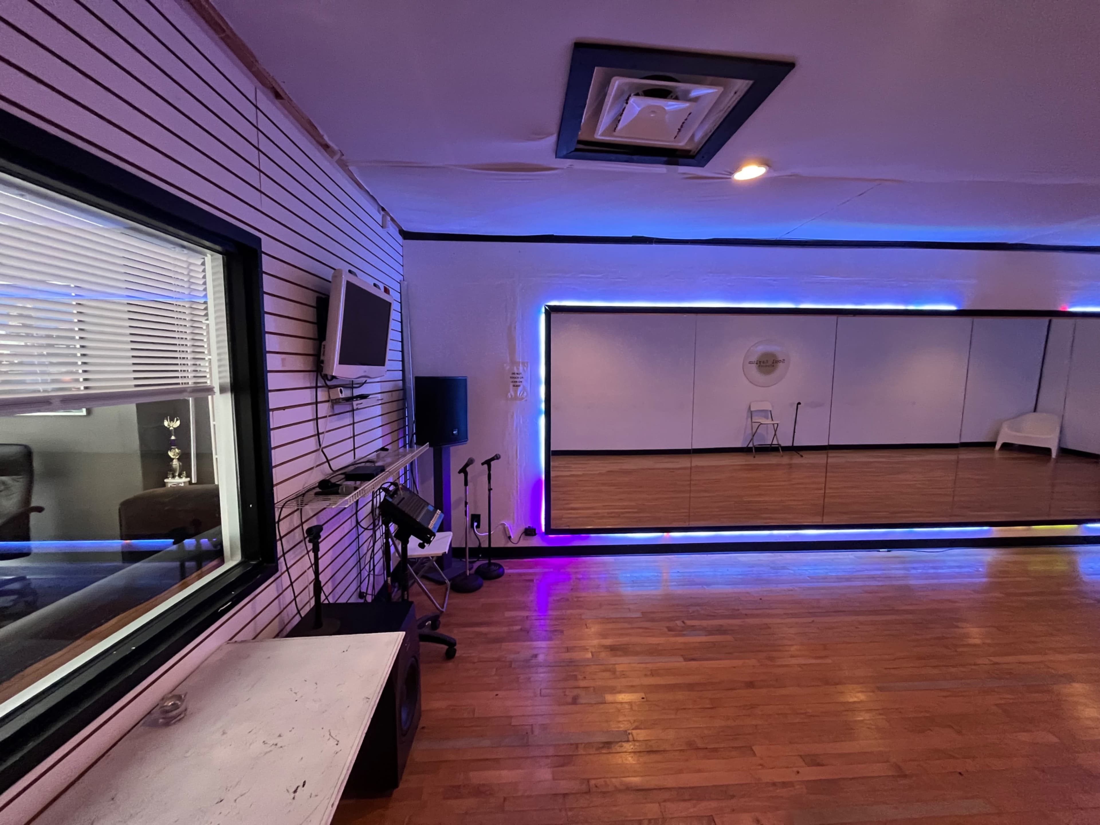 A recording studio with a mirrored wall, a television, and musical equipment arranged along one side.
