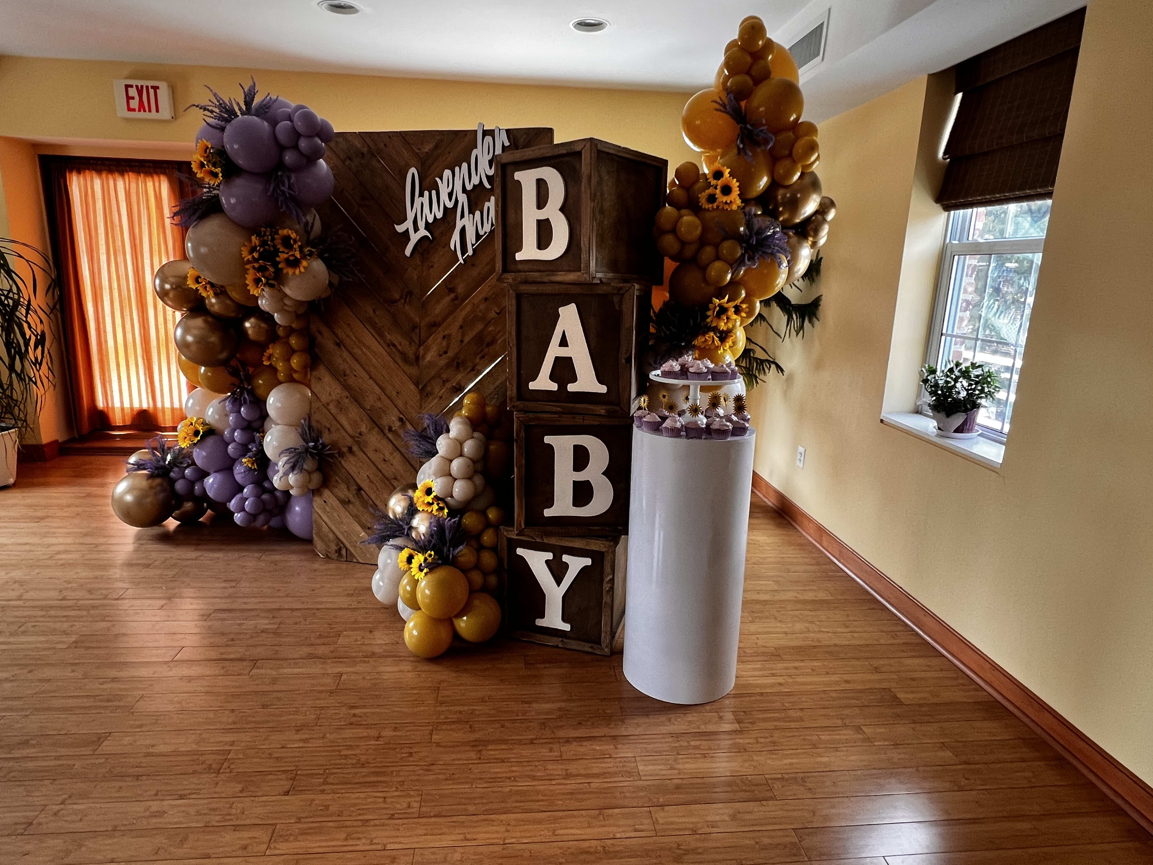 A gender-neutral baby shower is decorated with yellow, purple and brown balloons.