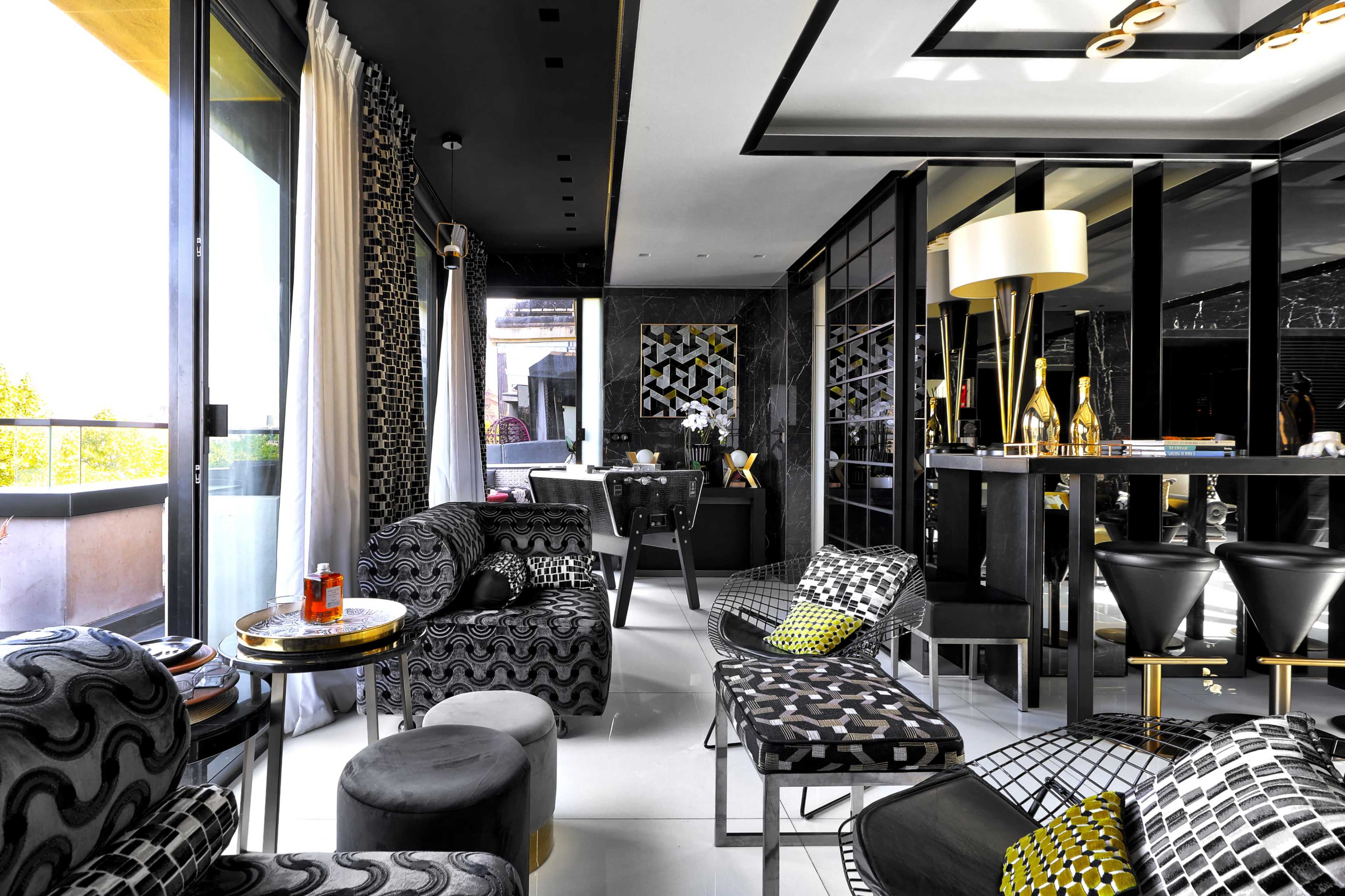 The image shows a modern, stylish interior of a lounge area featuring black and white patterned furniture, a bar section, and large windows letting in natural light.