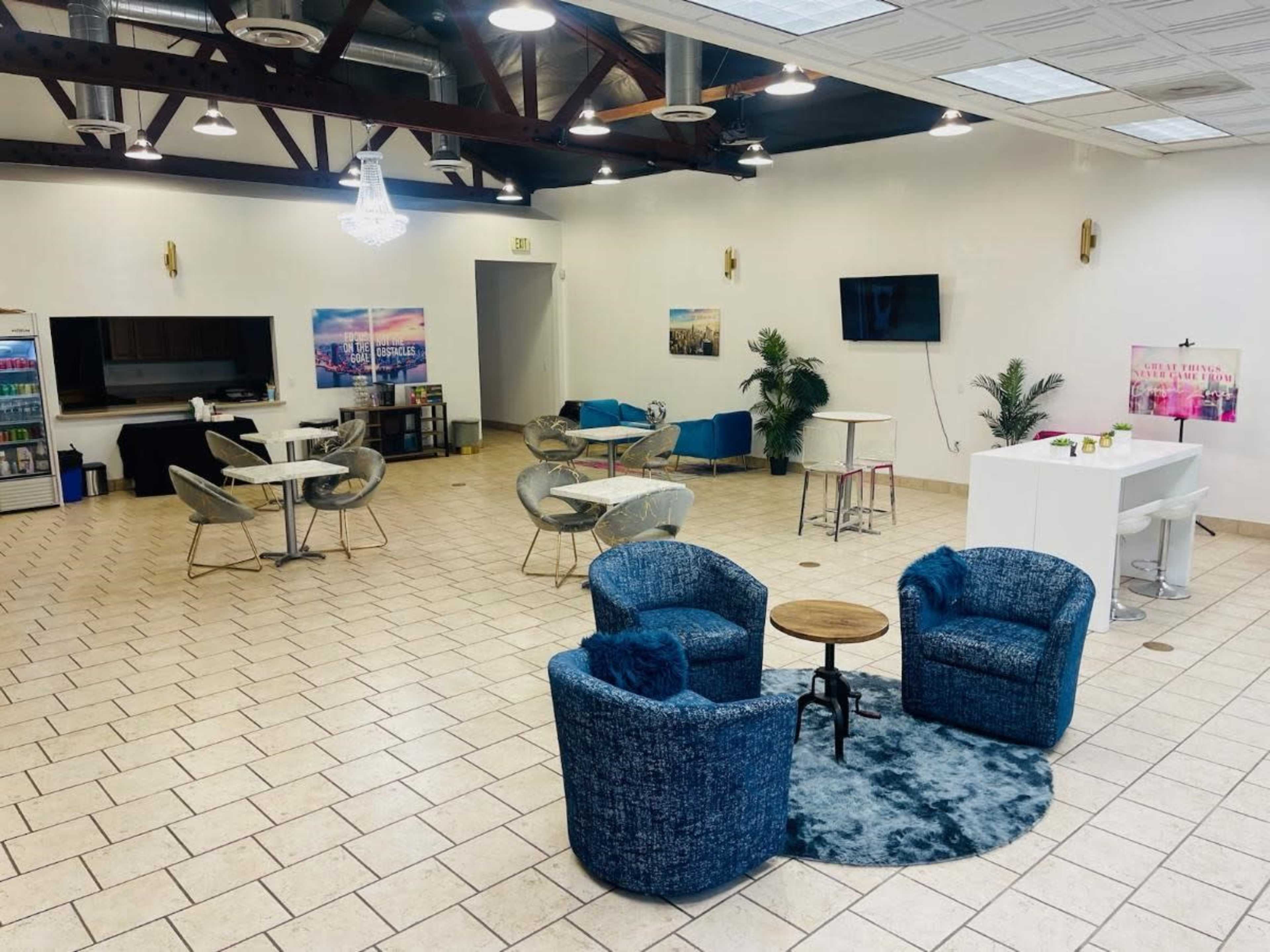 A spacious indoor area with seating, including two blue upholstered chairs and a small round table, surrounded by other furniture and decor.