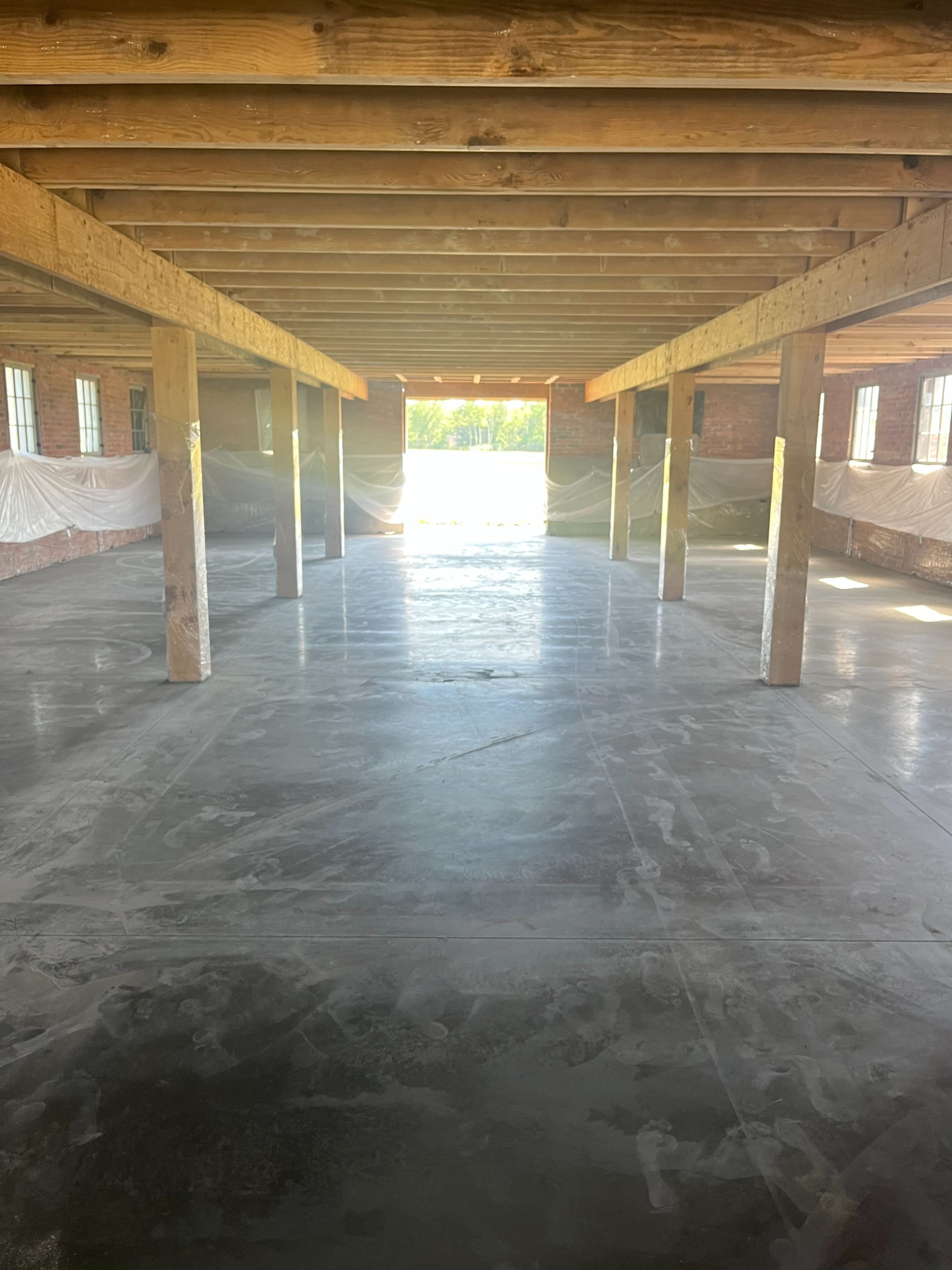 An unfinished interior space with exposed wooden beams and pillars, and a concrete floor leading to an open doorway.